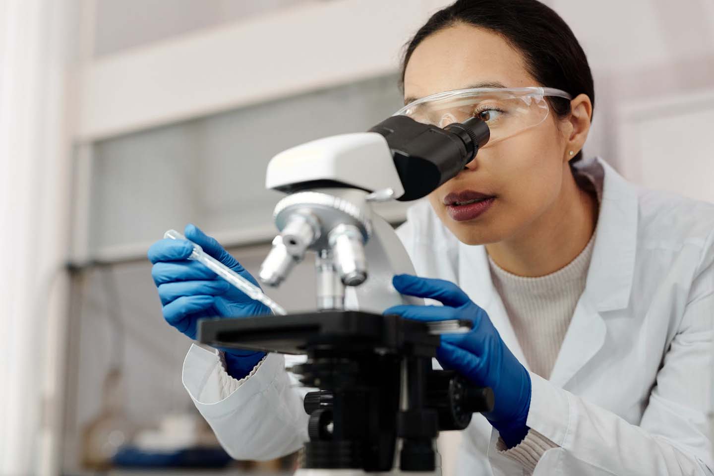 a woman using a microscope while wearing blue laboratory gloves