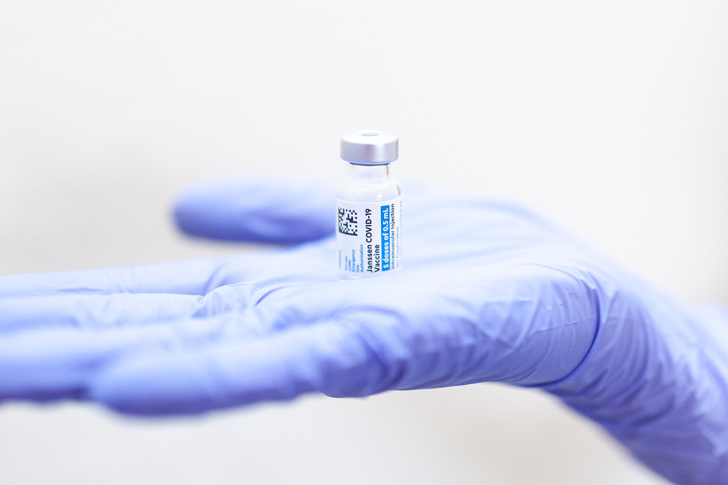 right hand with blue nitrile glove holding a vaccine vial