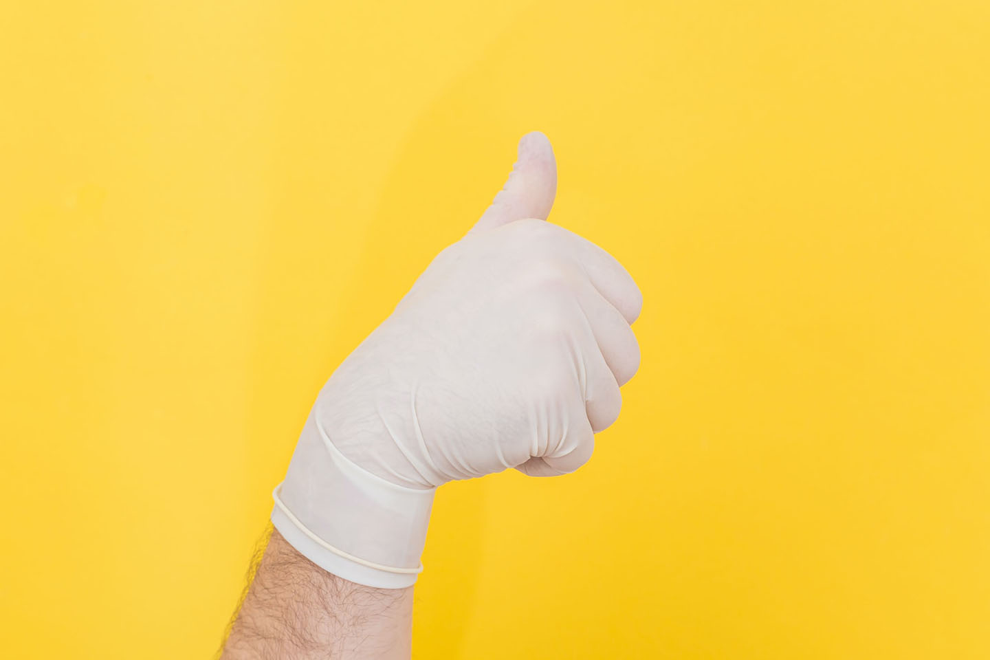 hand in white glove on yellow background giving a thumbs up