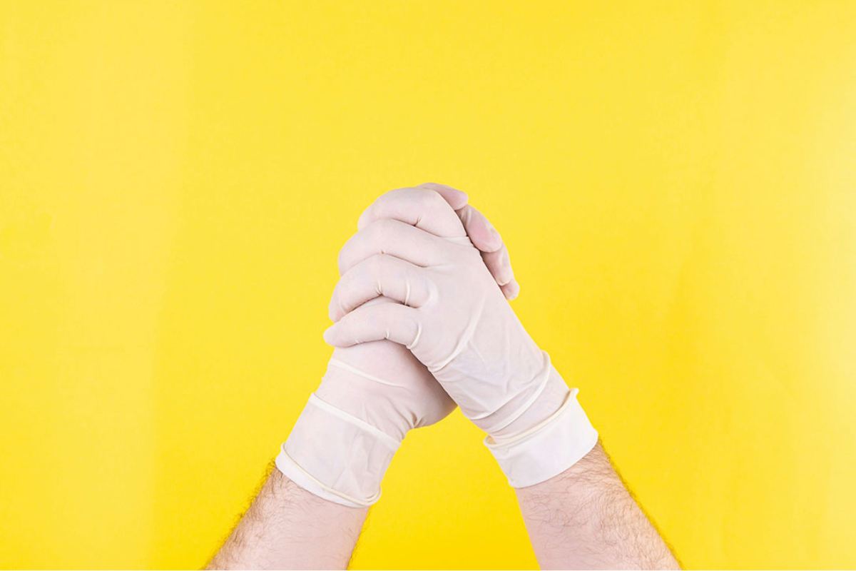 Gloved hands clasped in front of a yellow background