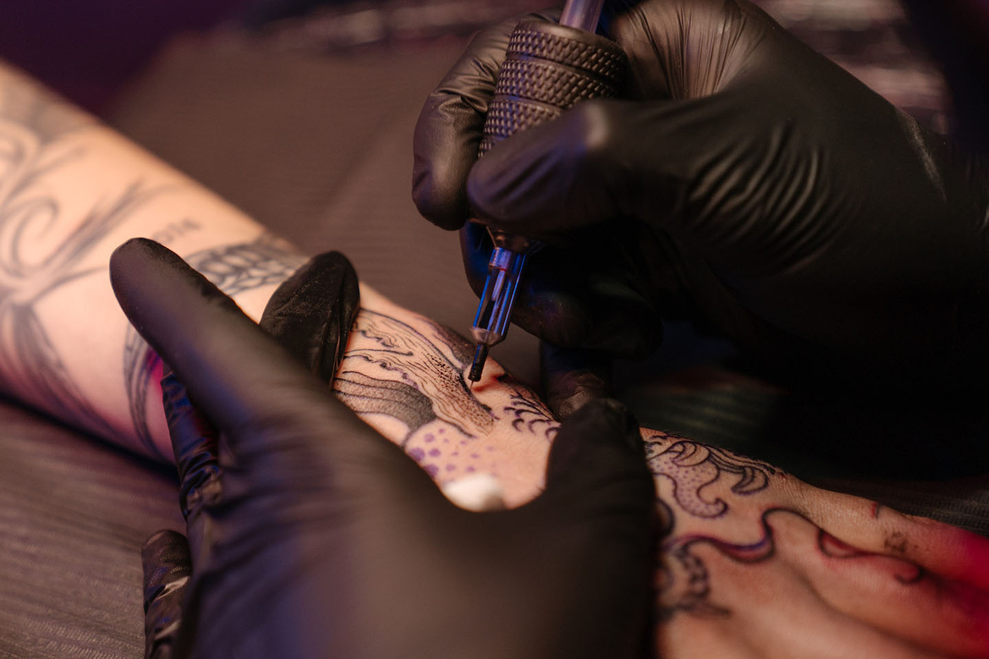 artist wearing black gloves while doing tatoo on a person's arm