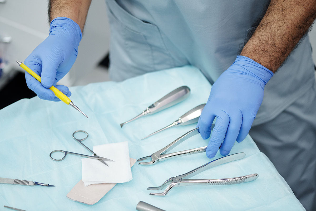 person in a surgical gown with gloved hands holding dental tools