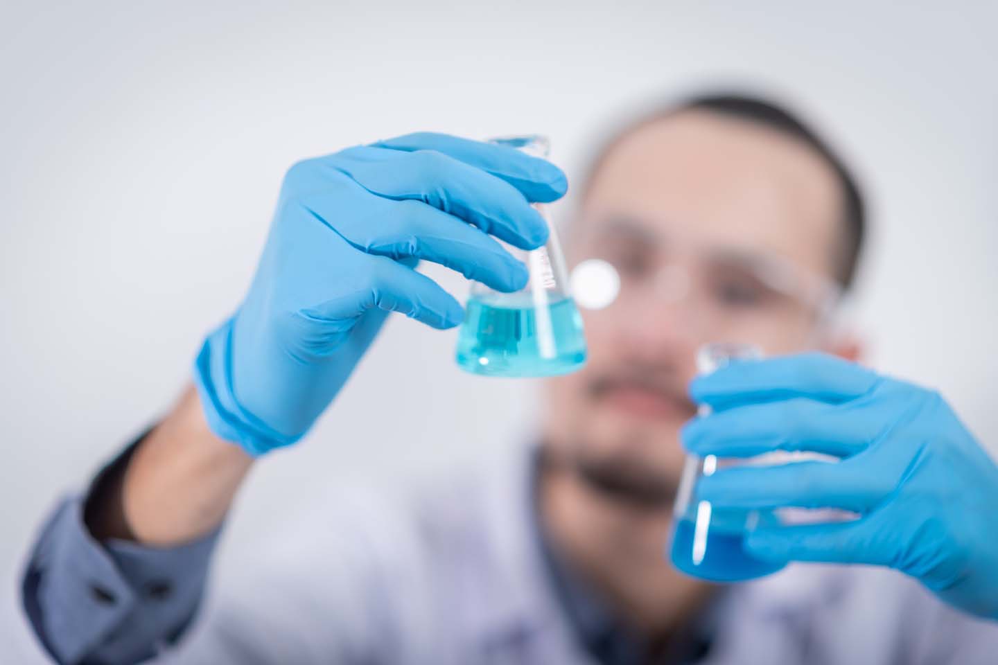 a chemist wearing blue gloves and holding glass flasks with chemicals