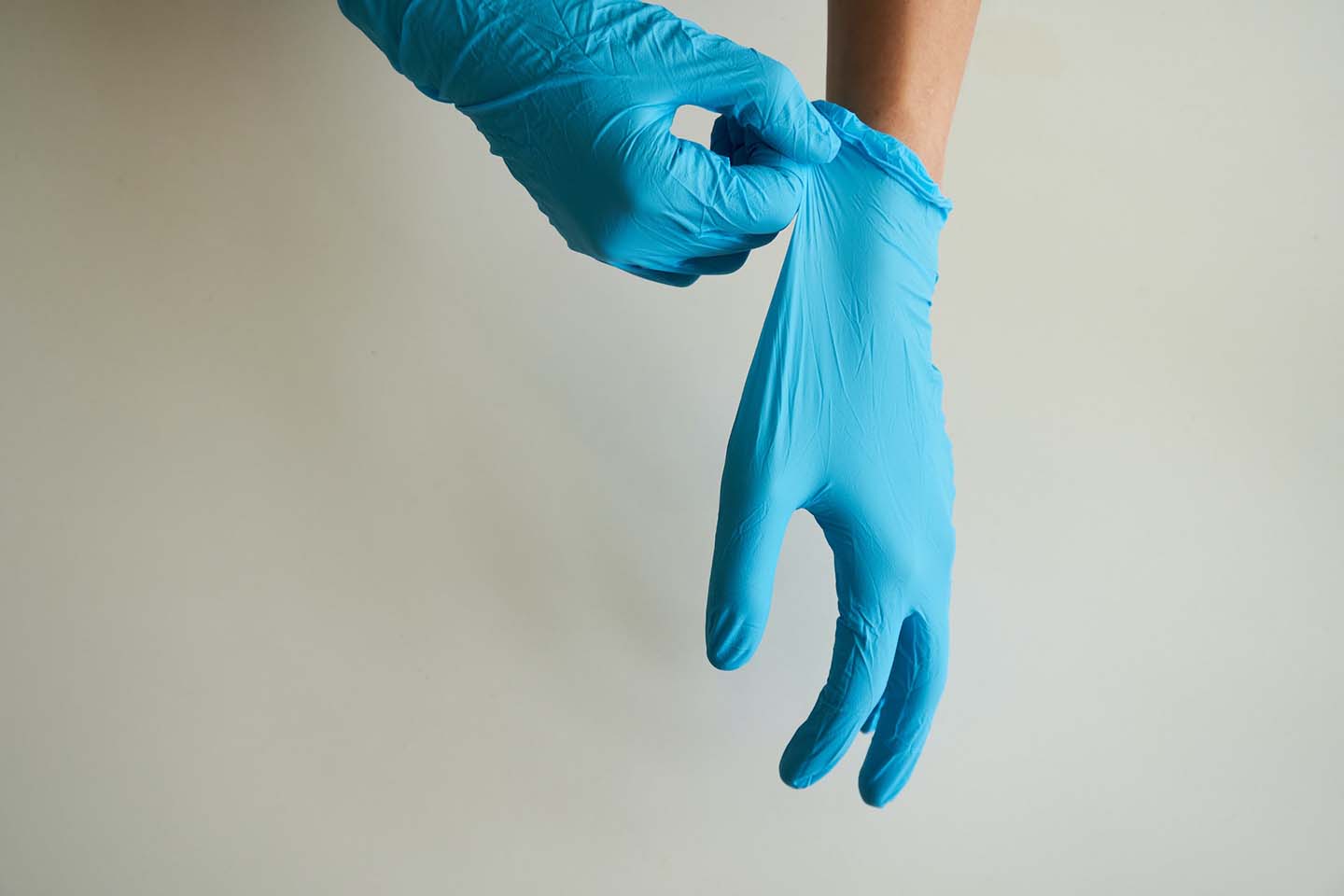 a person donning and pulling the blue nitrile gloves towards arm