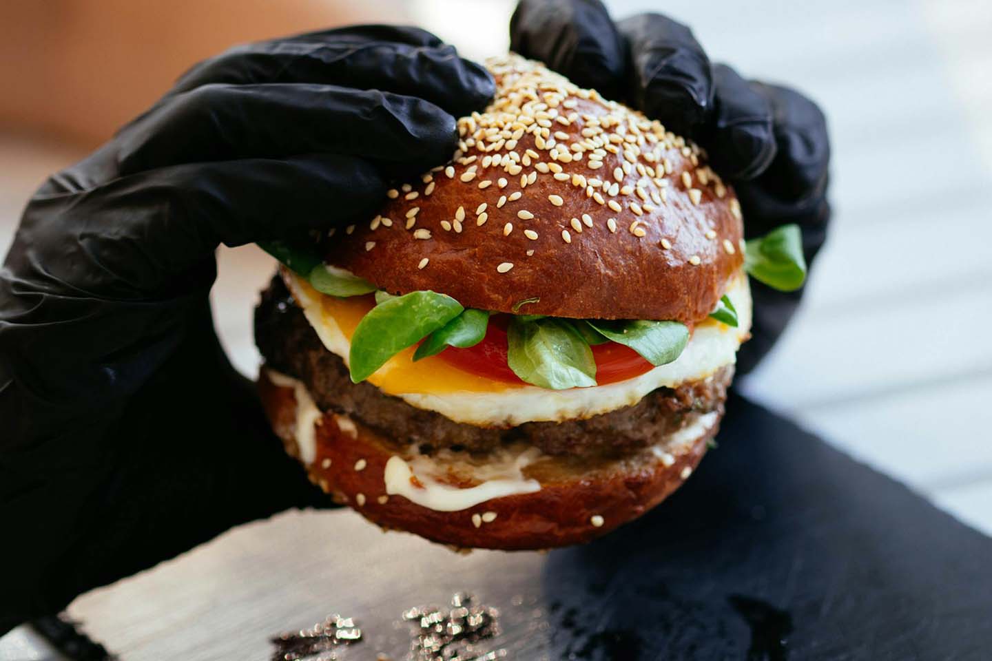 a person holding a burger while wearing black gloves