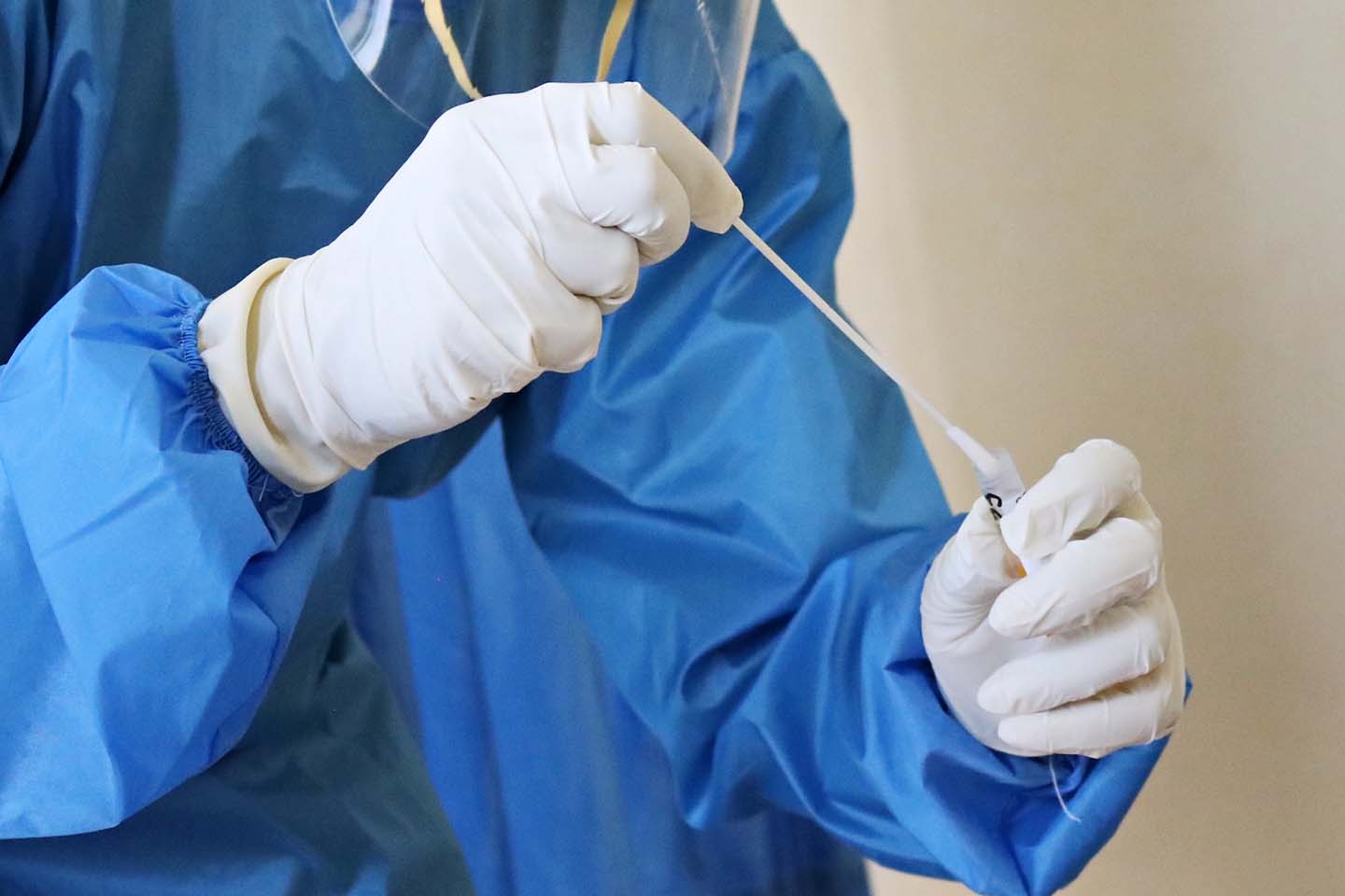 a medical professional wearing full personal protective equipment while collecting samples from a sterile tube
