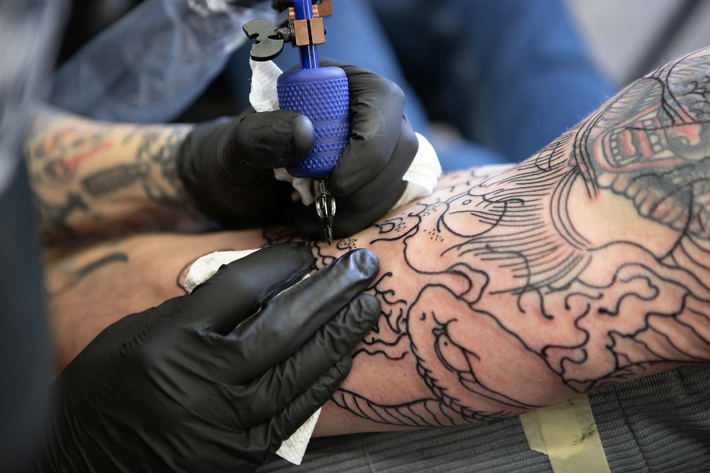 an artist wearing black gloves while tattooing on a client's right arm