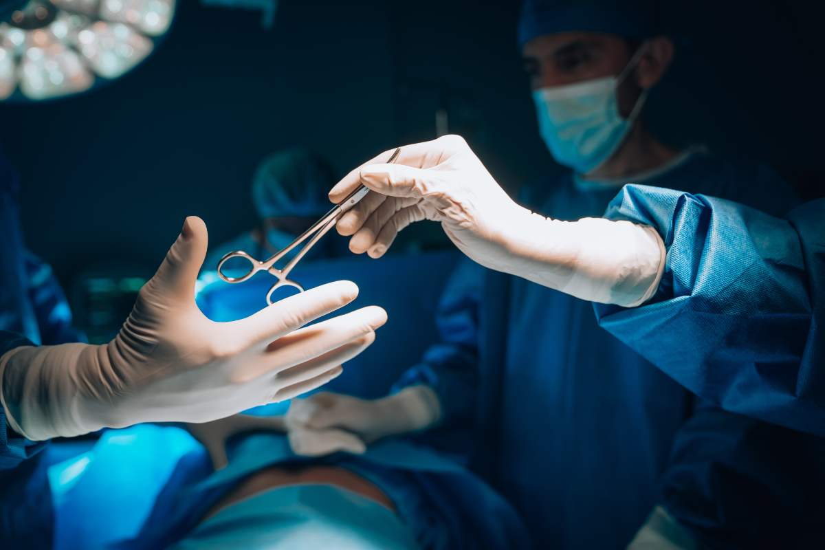 a surgical assistant passes a pair of sterile scissors to the surgeon during an operation