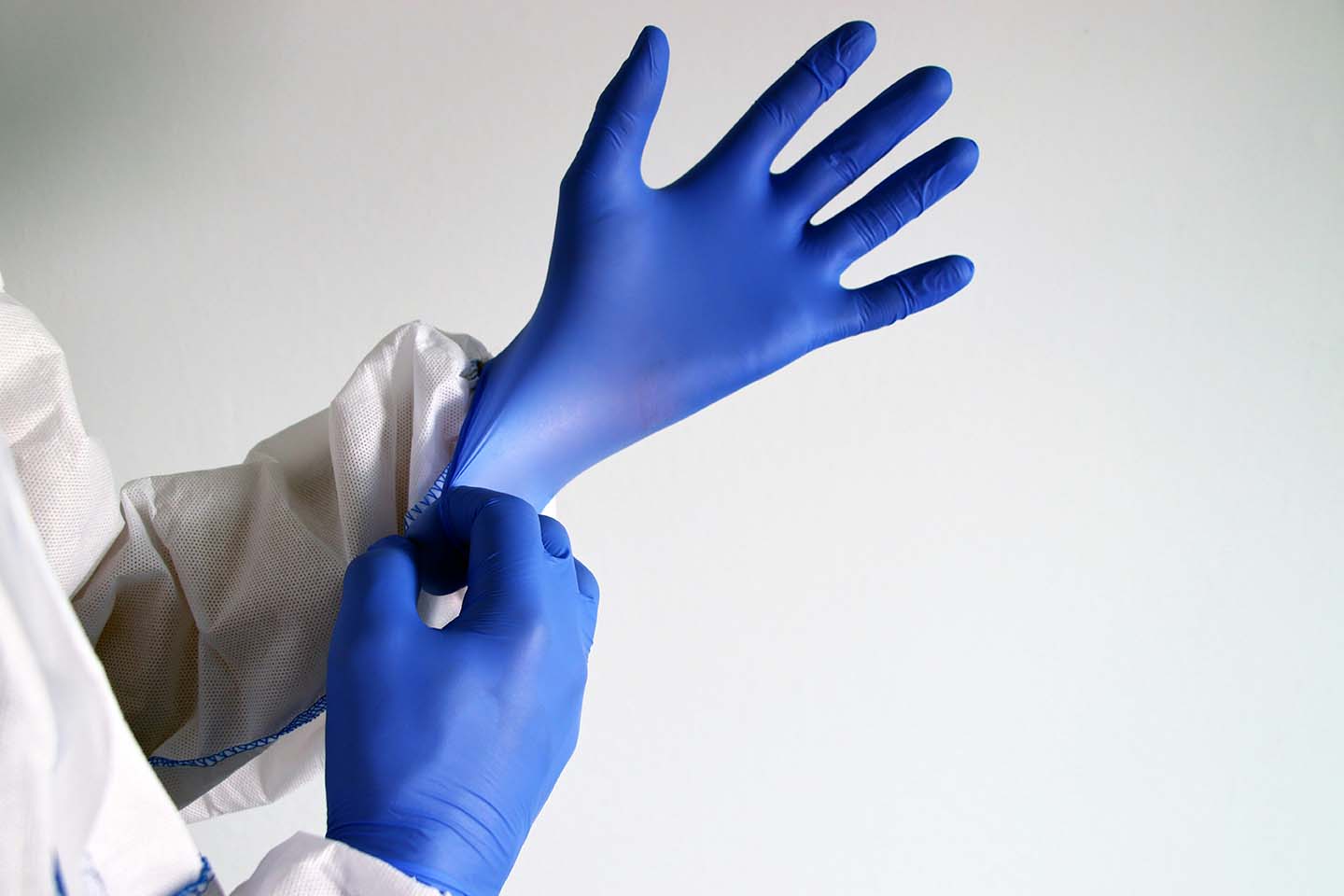 Two hands wearing a pair of nitrile surgical gloves, with a white lab coat covering the arms.
