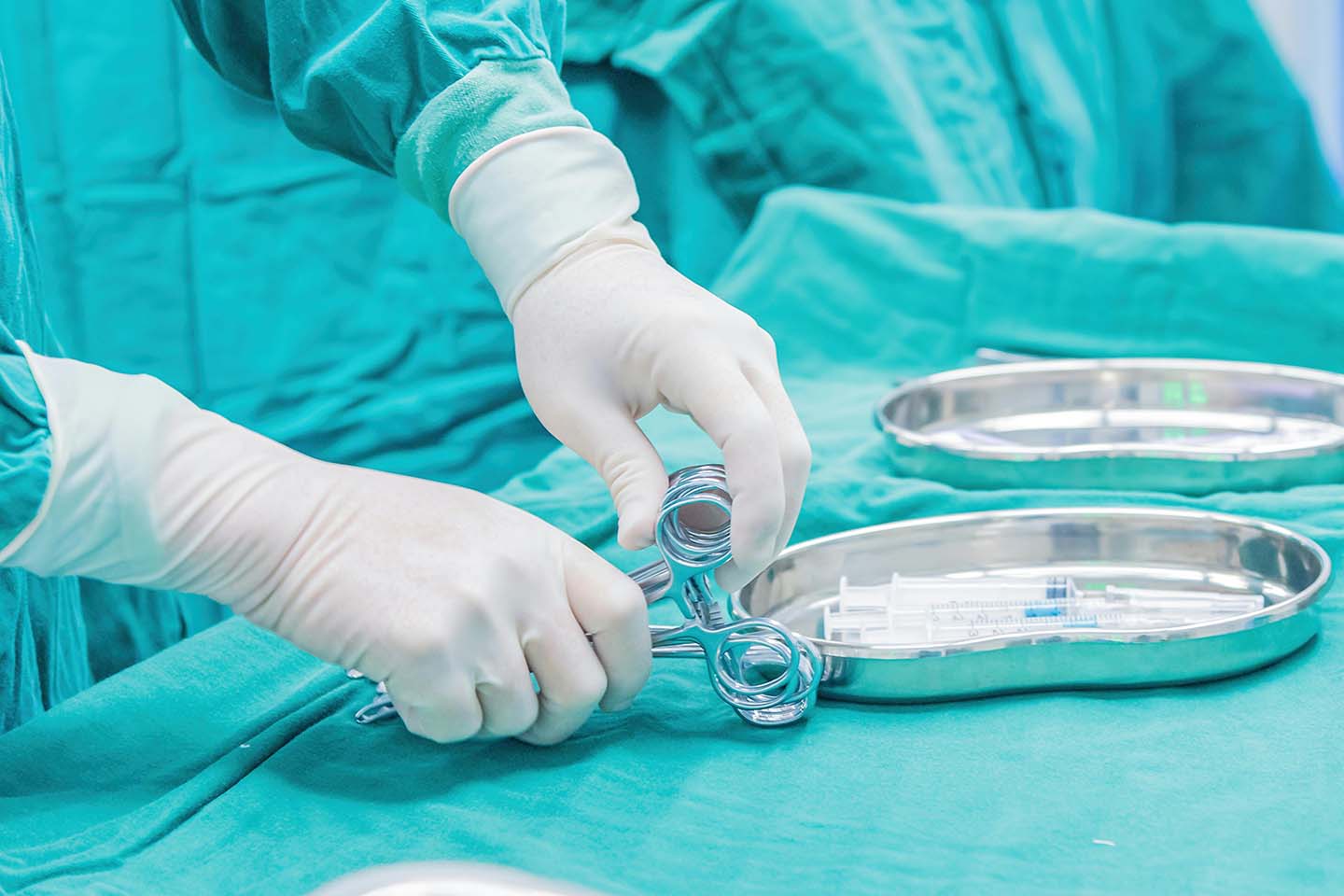 A medical professional wearing white latex surgical gloves while arranging several surgical scissors in the operating table.