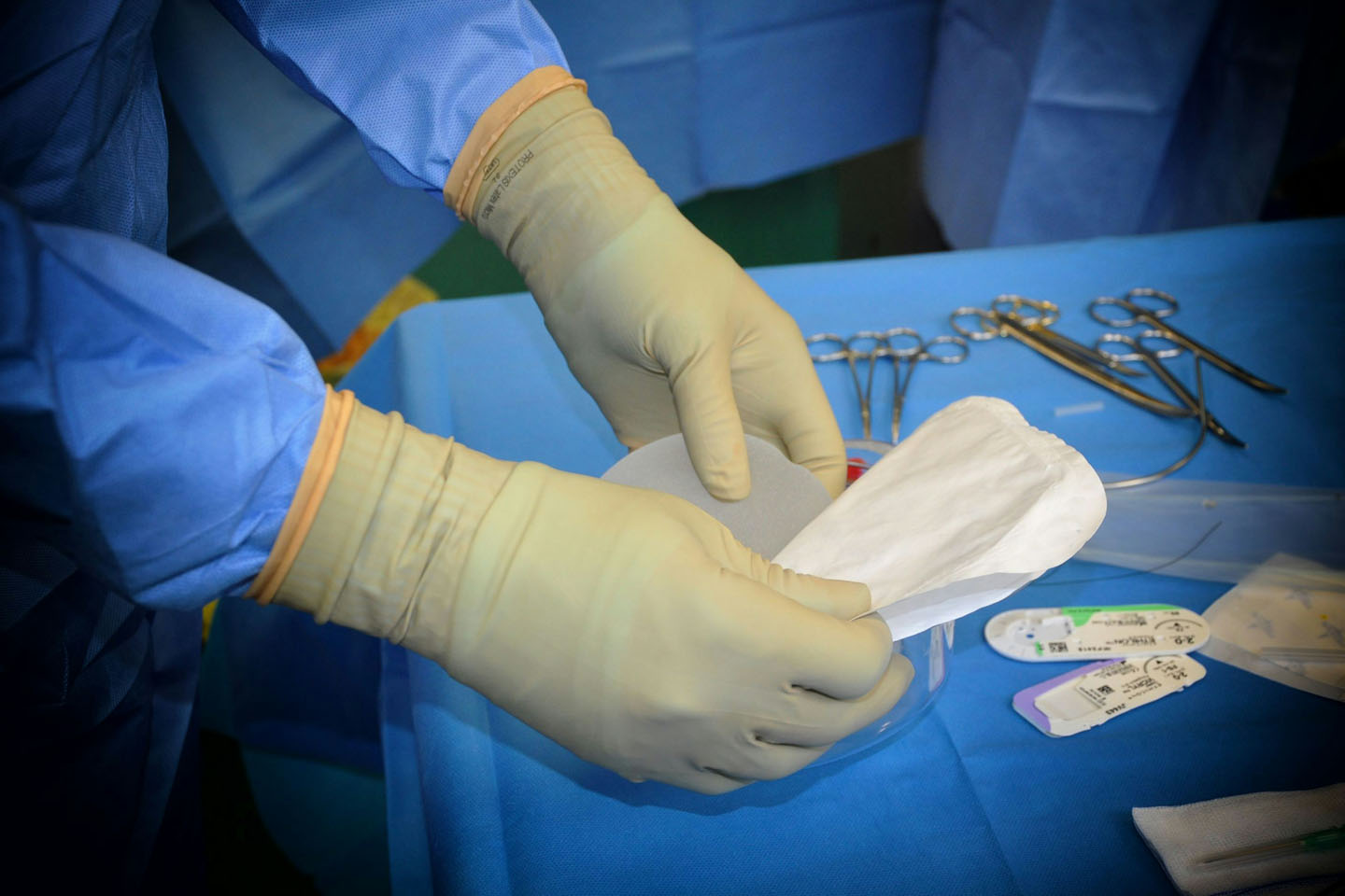 A surgical assistant wearing surgical gloves and organizing sterile tools and equipment in the operating table.
