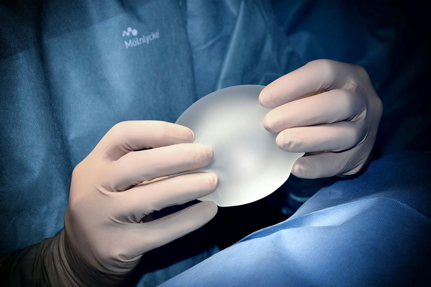 A plastic surgeon holding an implant while wearing white surgical gloves.