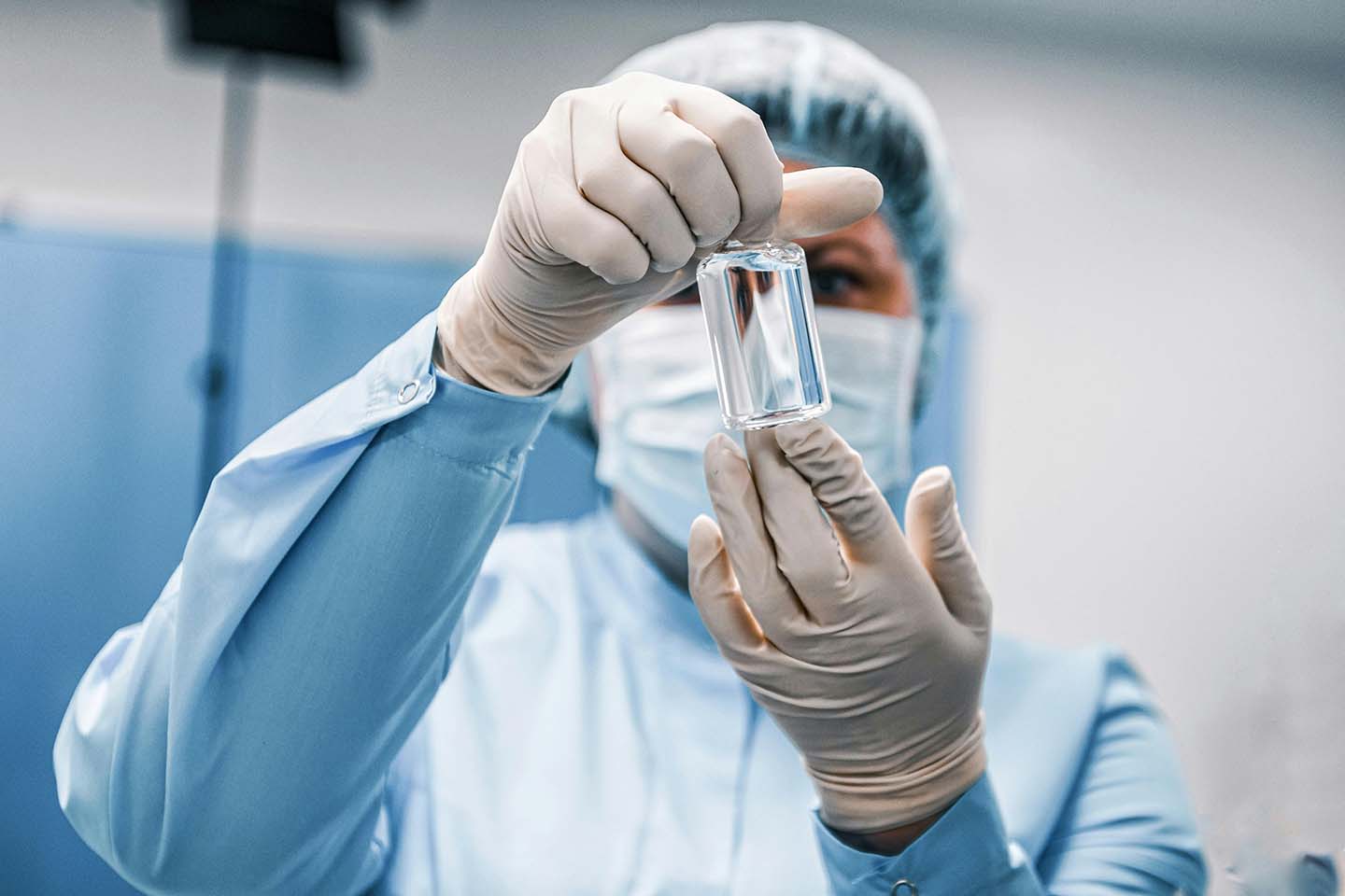 A surgeon wearing personal protective equipment and holding a vial at her eye level.