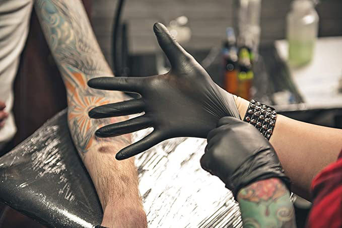 a tattoo artist donning a pair of disposable black gloves