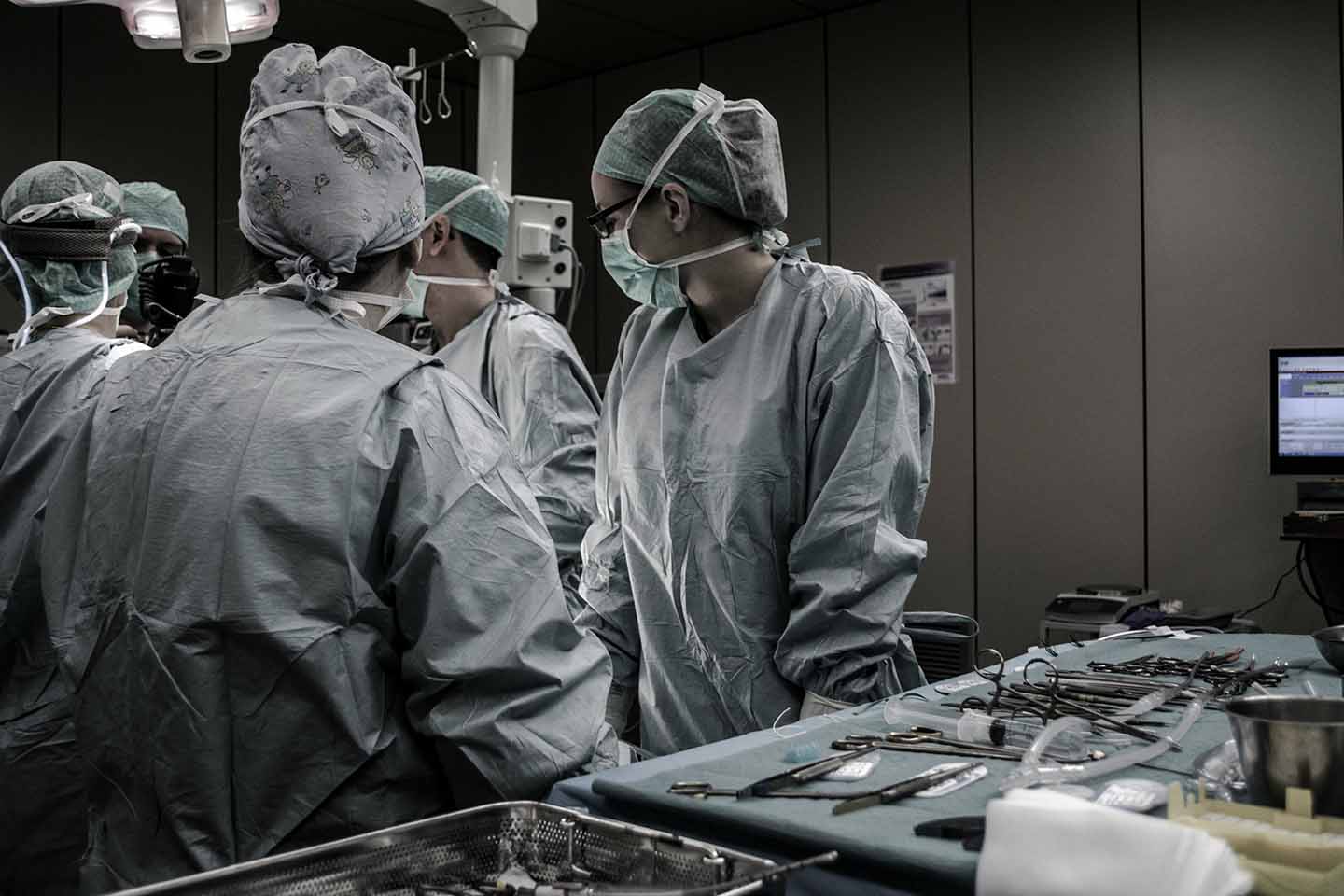 surgeons in PPE stand in operating theatre with medical equipment around them.