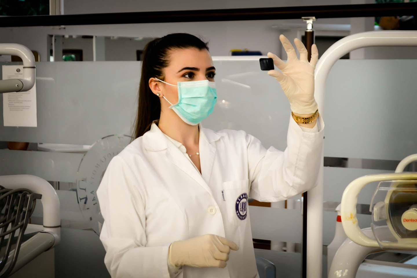 Woman in lab coat and medical gloves looks at a slide in the light in a lab.