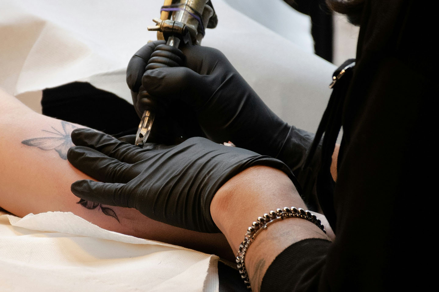Tattoo artist wears black gloves while tattooing butterflies on customer.