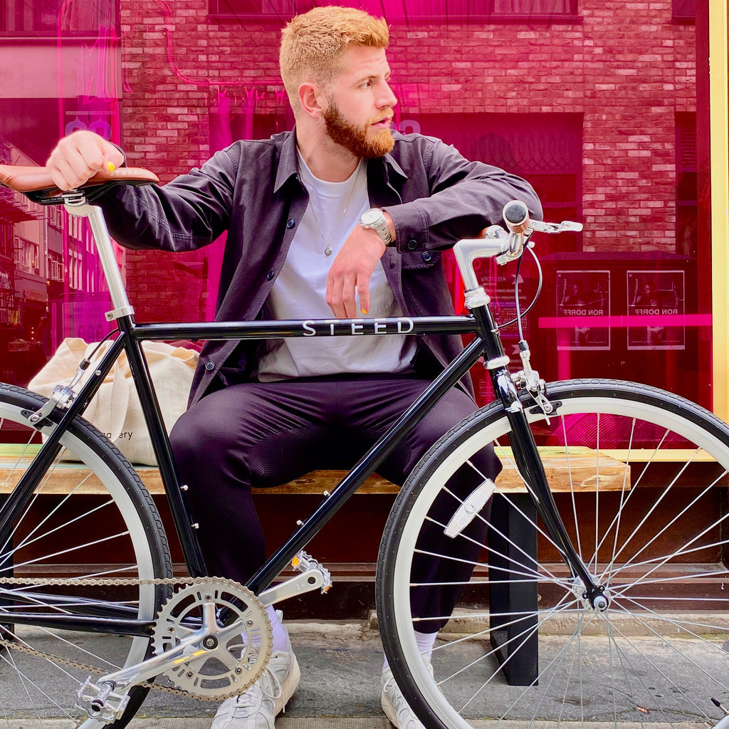 man with ginger hair and beard sitting holding a onyx black single speed bike Thoroughbred Steed Bikes