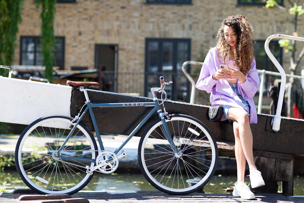girl in lilac shirt holding phone sitting next to atlantic blue Steed Bike
