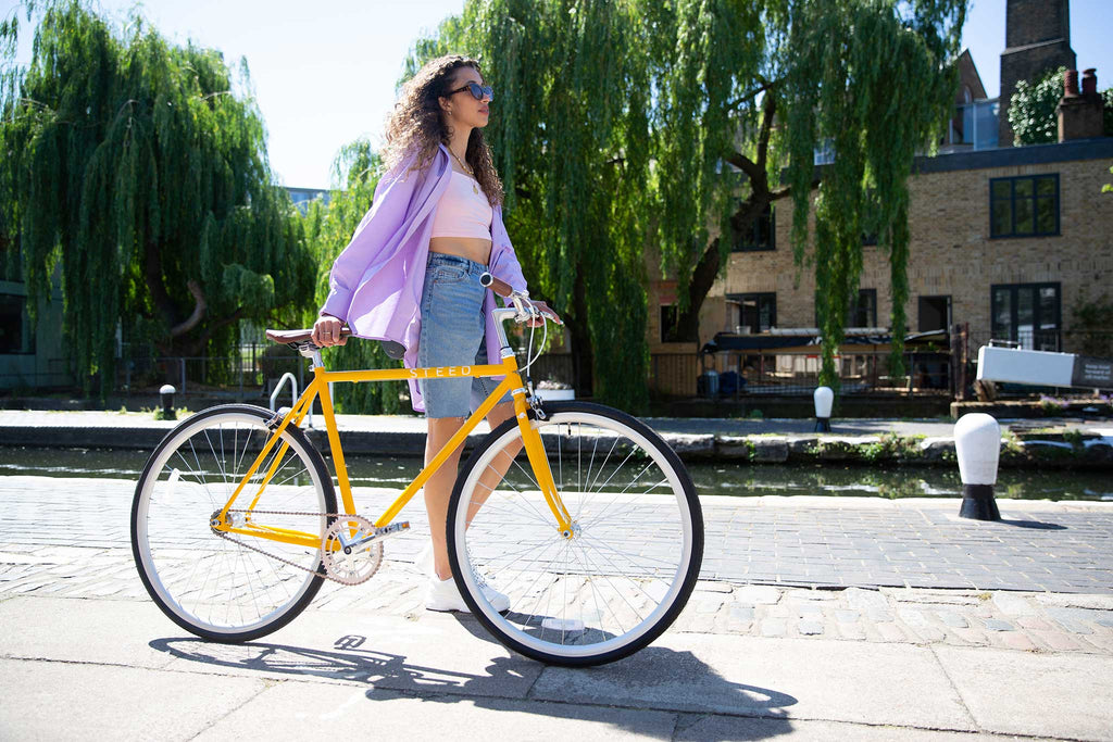 woman walking along canal with yellow fixie bike Steed Bike