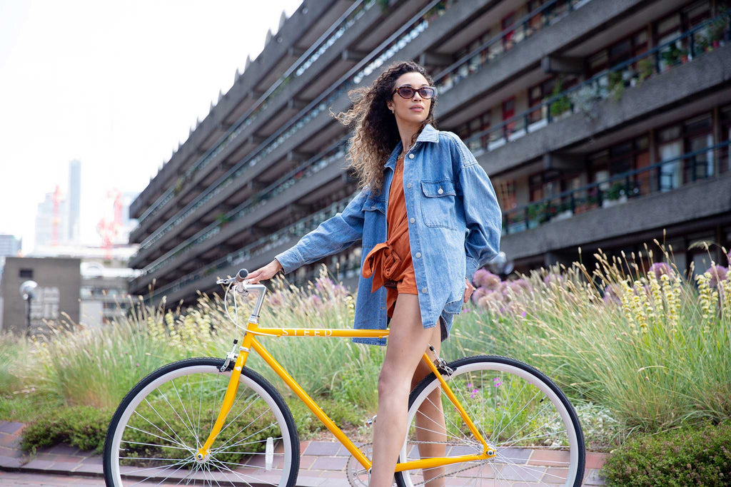 Girl on yellow single speed bikes wearing orange dress and denim jacket