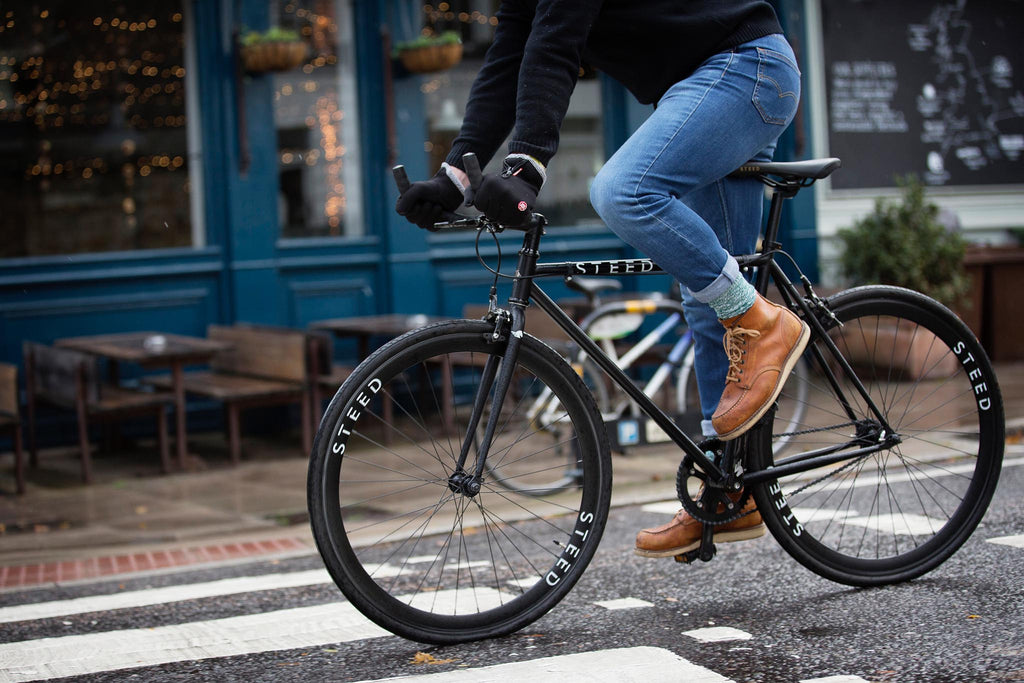 Man riding black single speed bike steed bike with blue jeans and brown boots