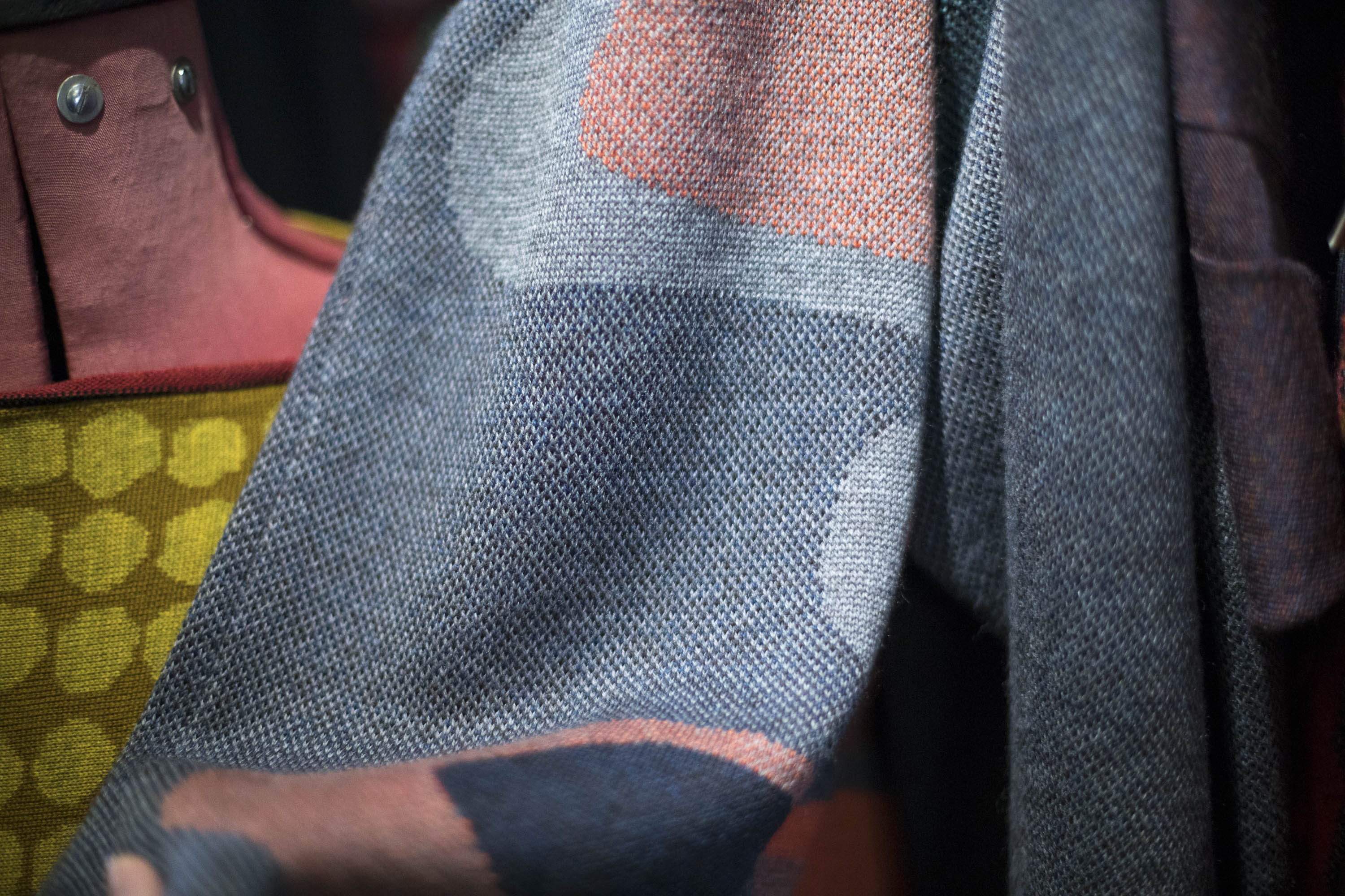 Close detail of knitted textile in three colours, which overlap to create abstract motifs and shape. Coral, grey and dark blue.