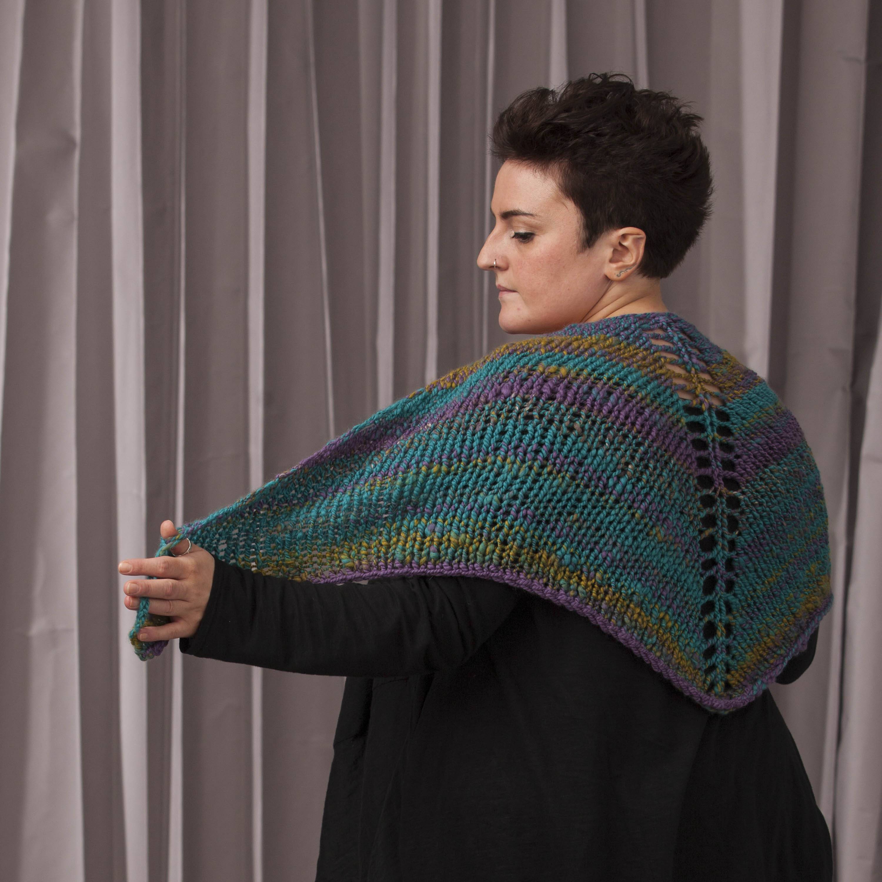 A woman wears a simple, handknit shawl made from handspun, multicoloured yarn