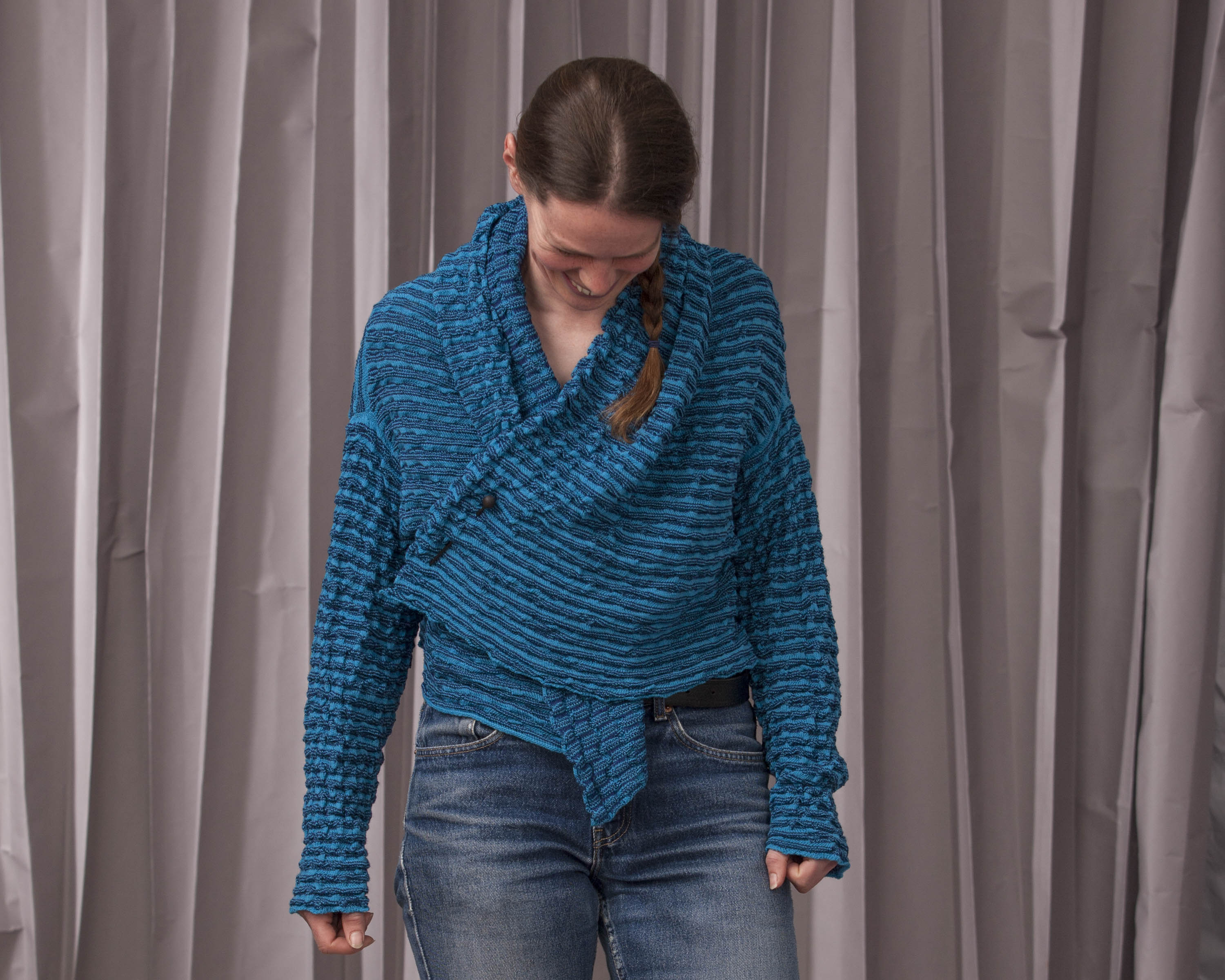 Model wears a contemporary knitted open jacket in bright blue, softly ridged textile