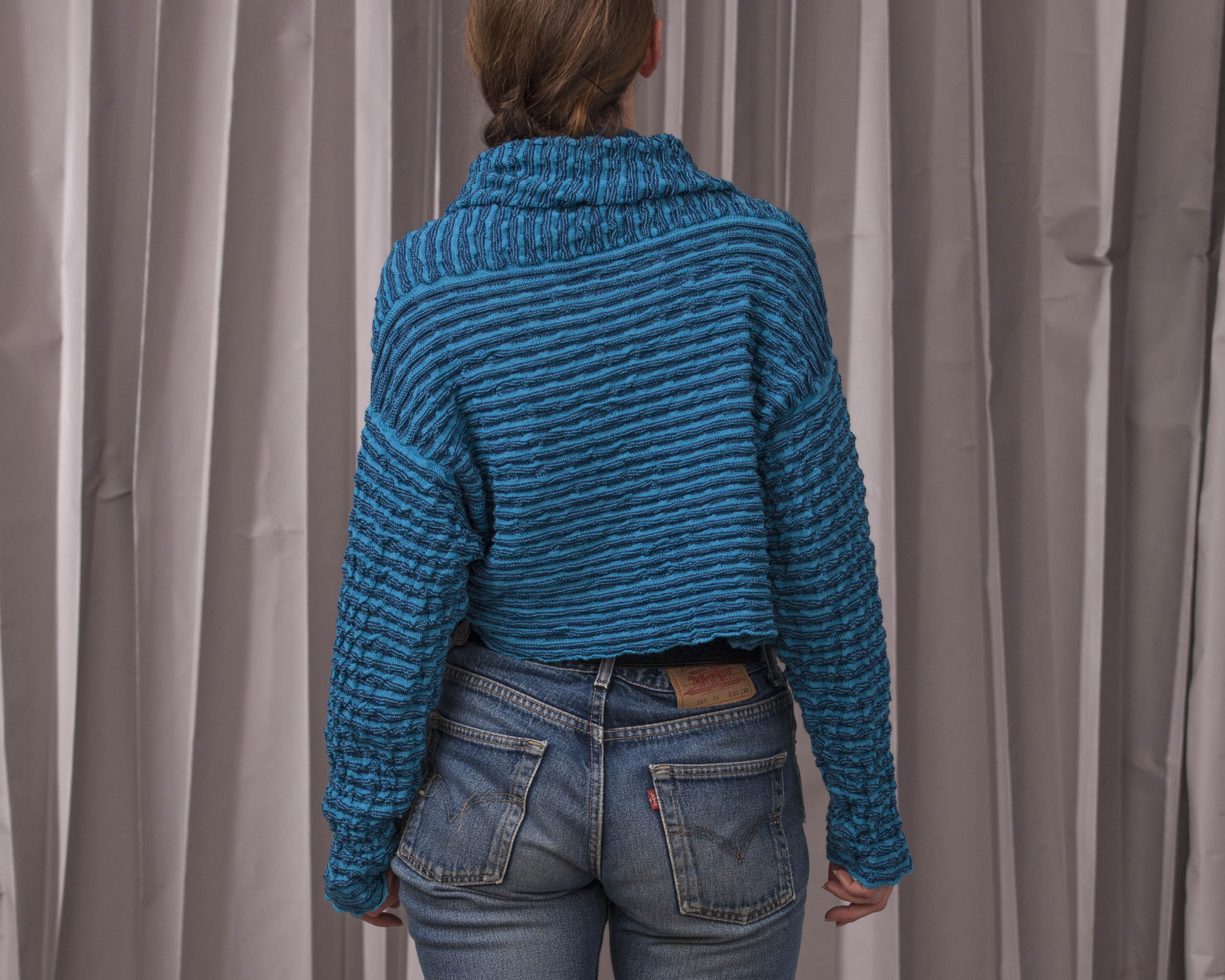 Contemporary Scottish knitwear, jacket seen from the back. Softly ridged, blue open jacket in a slouchy style with cowl neck