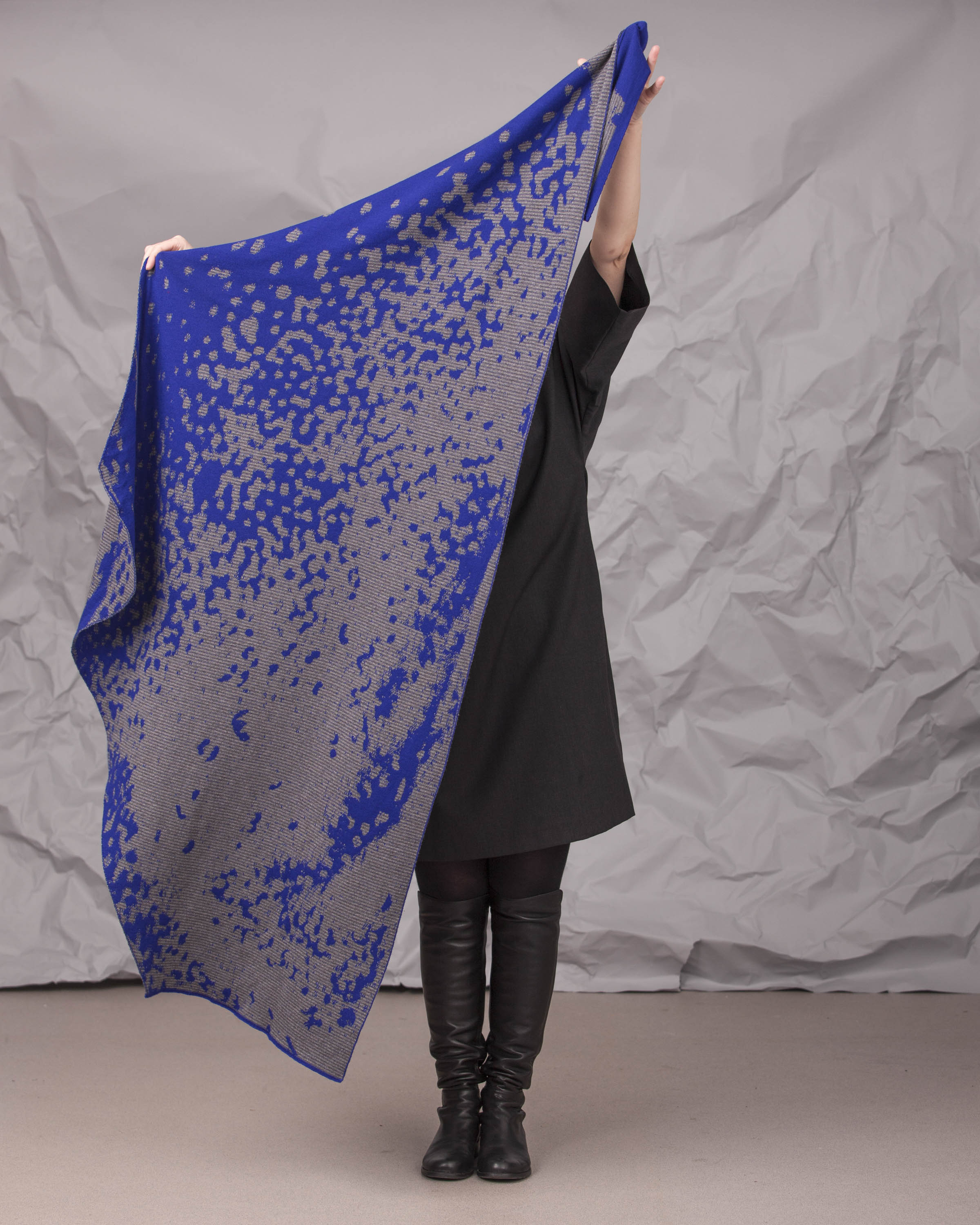 Model holds up a Marlet wrap lengthways - a large asymmetric shawl in bright blue and grey