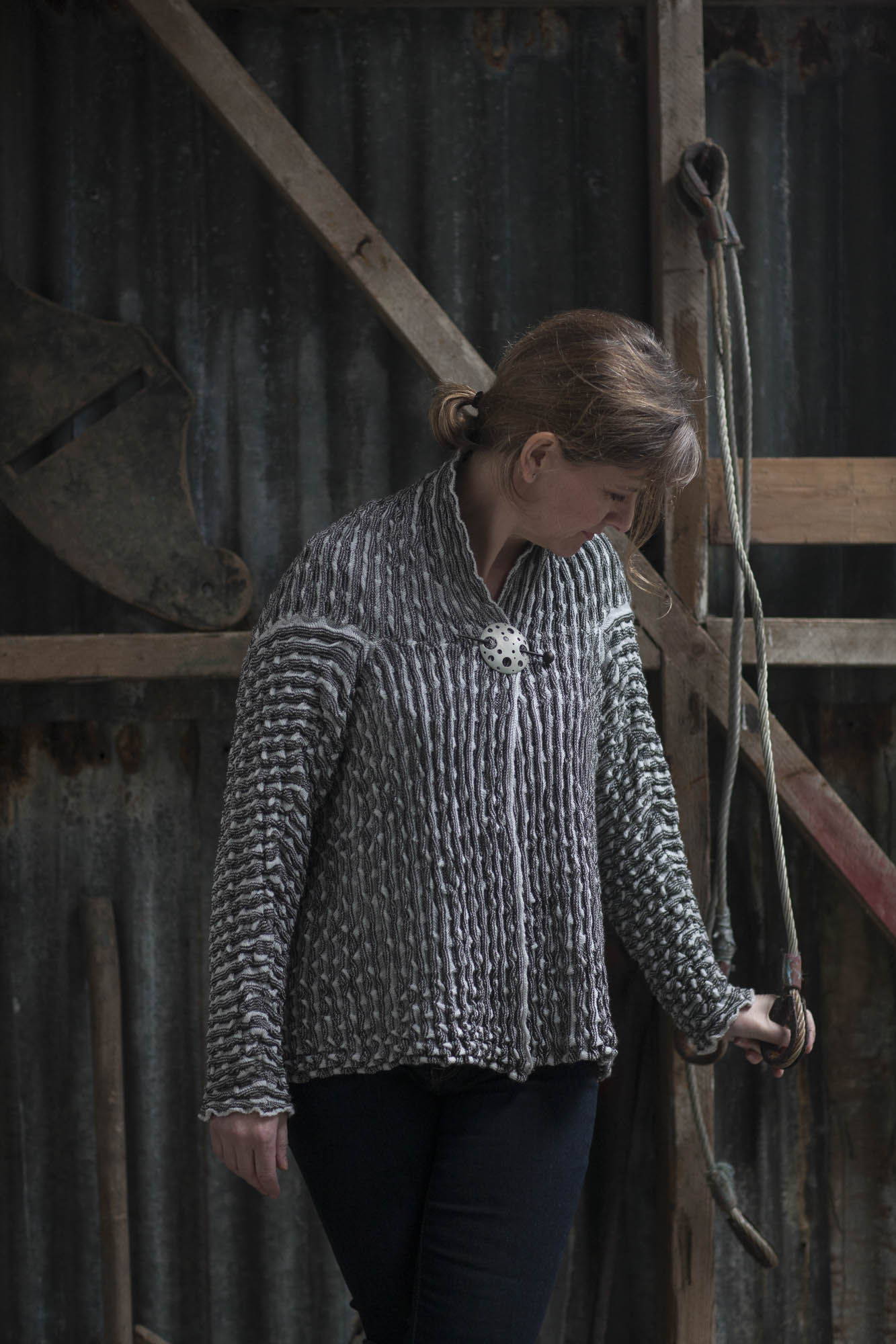 Modern Shetland knitwear - model wears ridged knitted jacket in chalky white and greys, pinned at neck