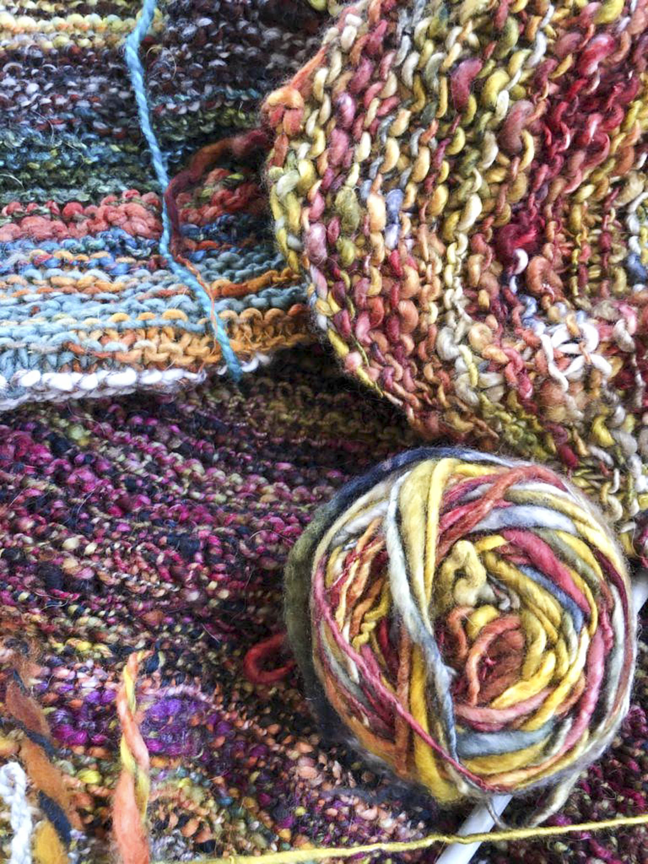 A ball of multicoloured, handspun art yarn - sitting on some knitting in the yarn