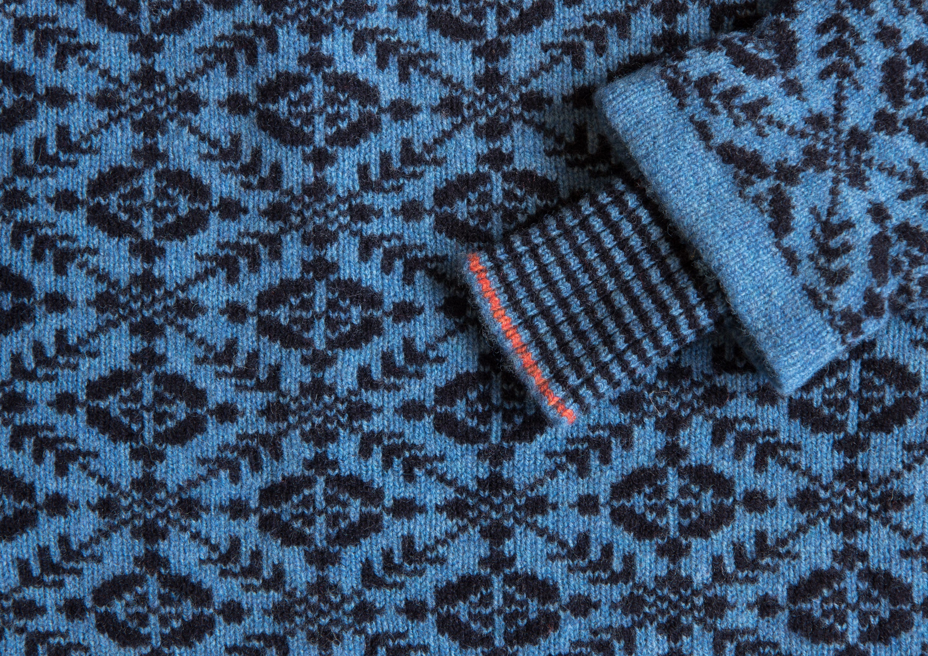 Detail of a real Fair Isle jumper, made in the Shetland Islands, Scotland. With inset storm cuff. Shown as a close up. The jumper is patterned all over in a traditional Fair Isle motif, in navy and blue, with a cuff detail stripe in coral