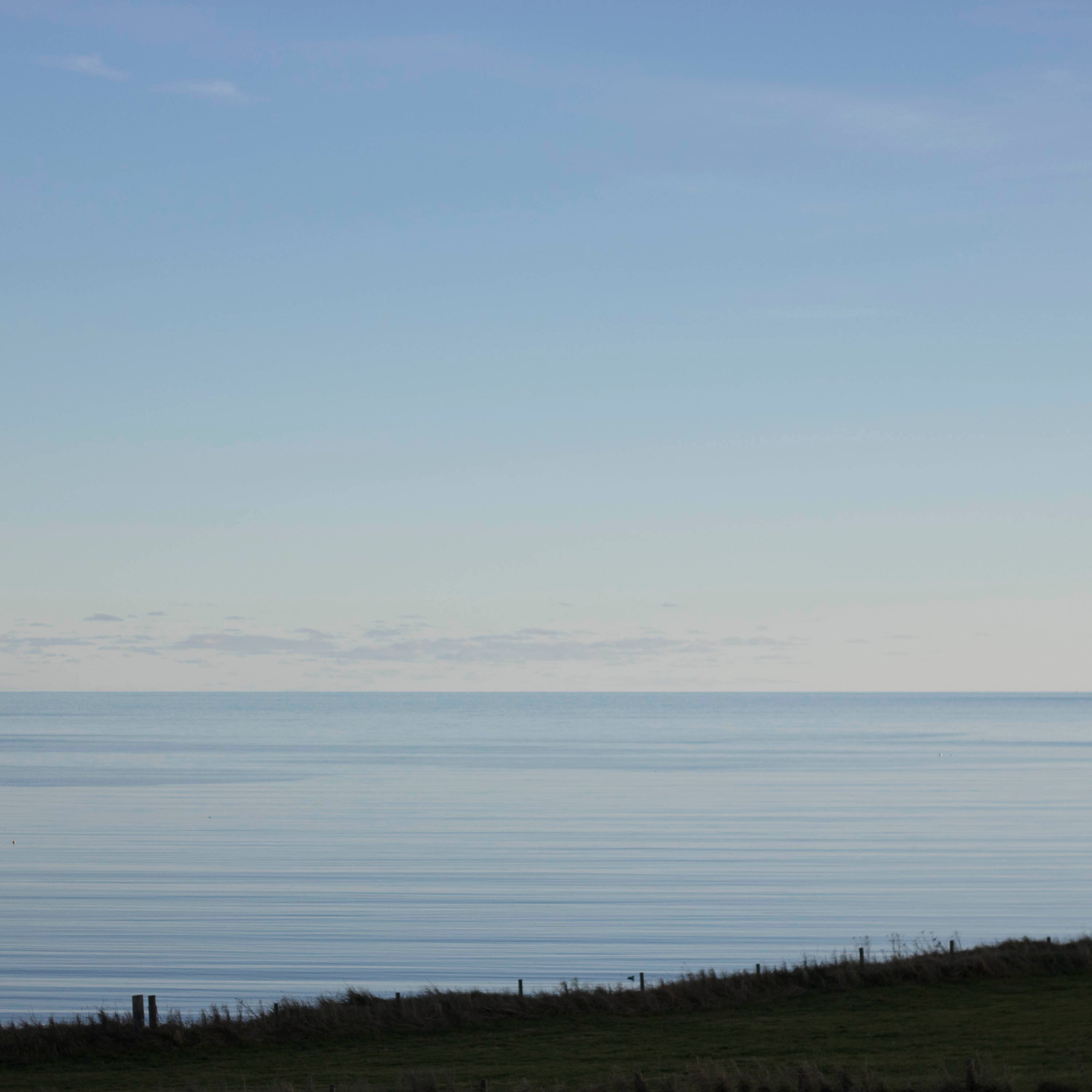 Looking out over a grassy field, at twilight, to a very still sea at Hoswick, Shetland