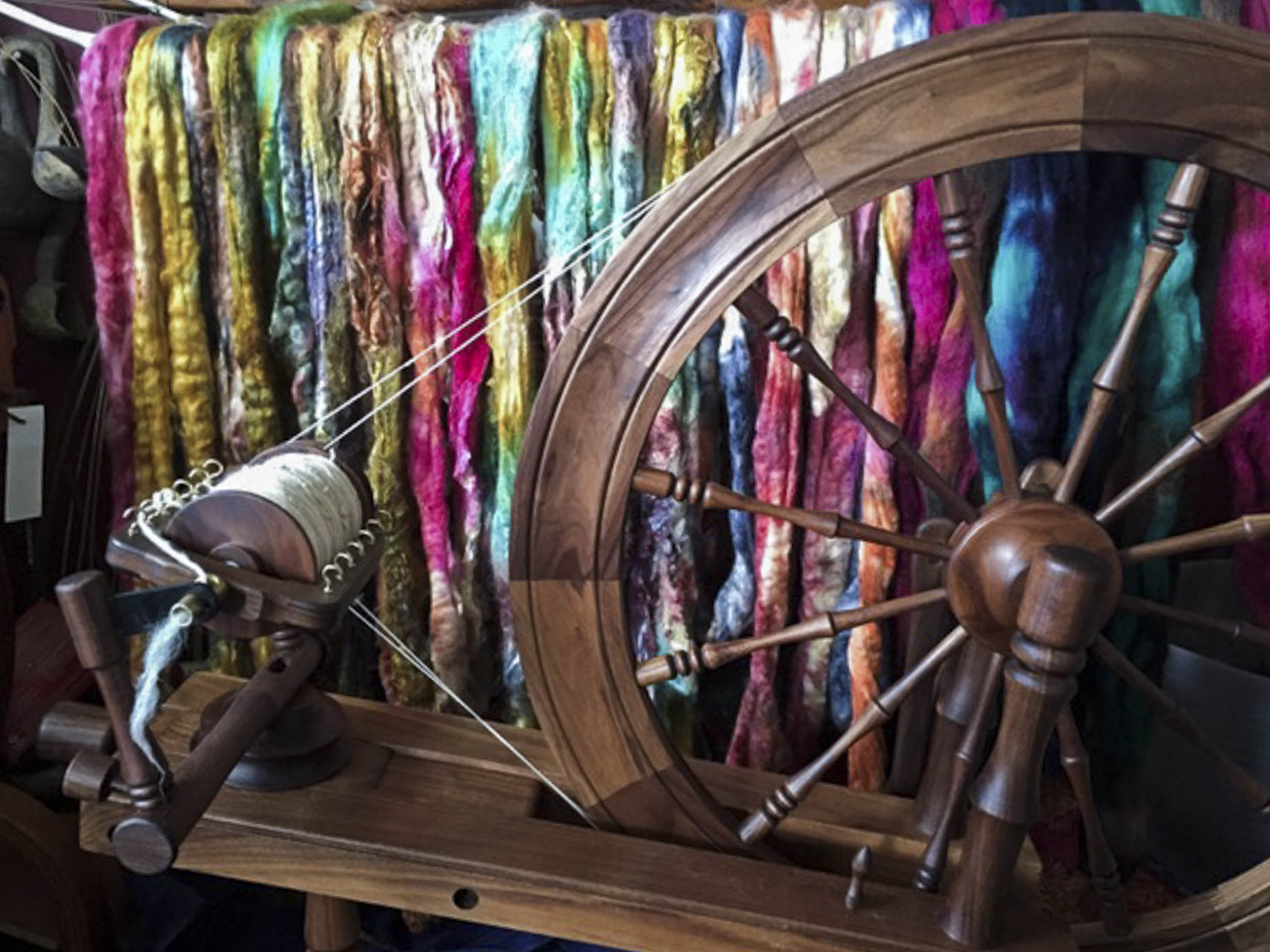 A wooden spinning wheel in front of brightly coloured, dyed fibre, drying