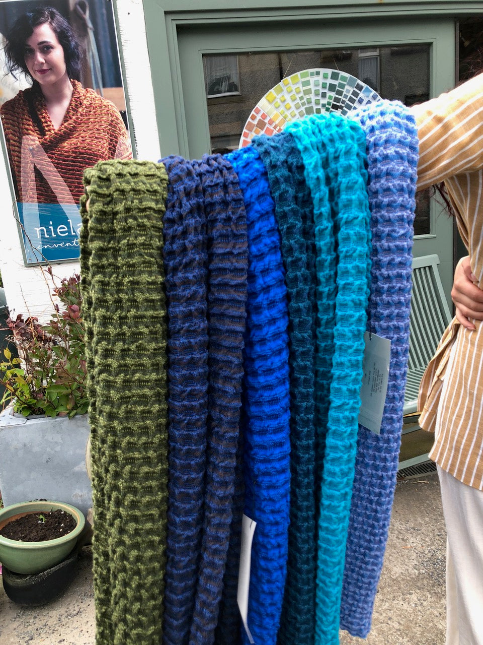 Holding out an armful of Rigg wrap scarves, outside the Nielanell contemporary knitwear studio, Shetland.