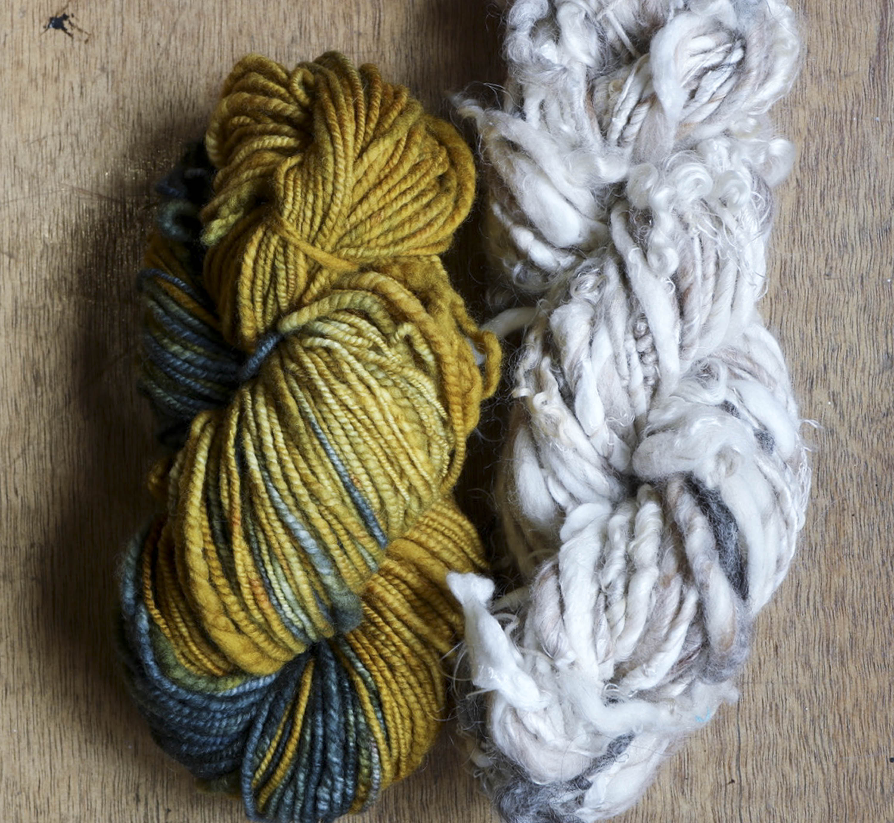 Two skeins of handspun art yarn. One in yellows and teals, the other in natural, pale greys