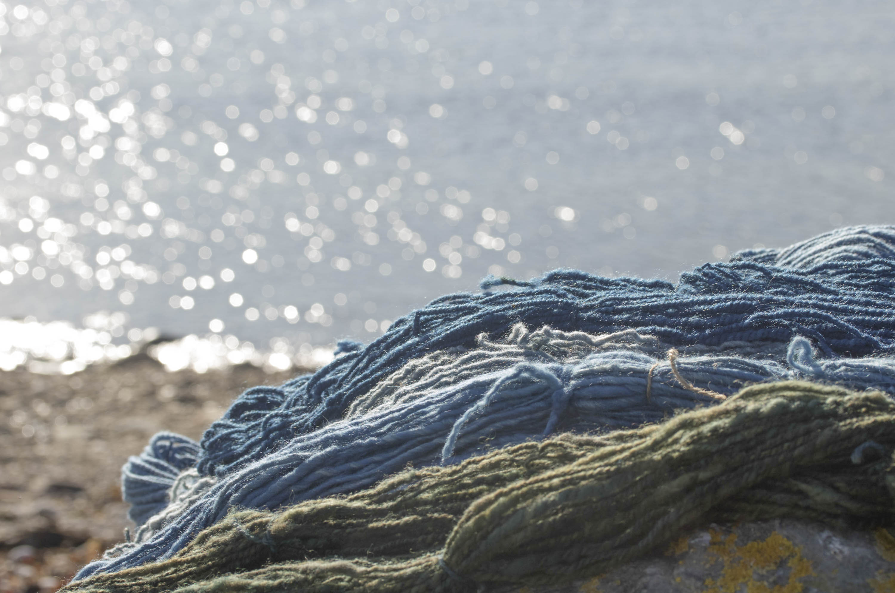skeins of handspun yarn on a rock on the shore at Hoswick, Shetland, with a sparkling sea in the background