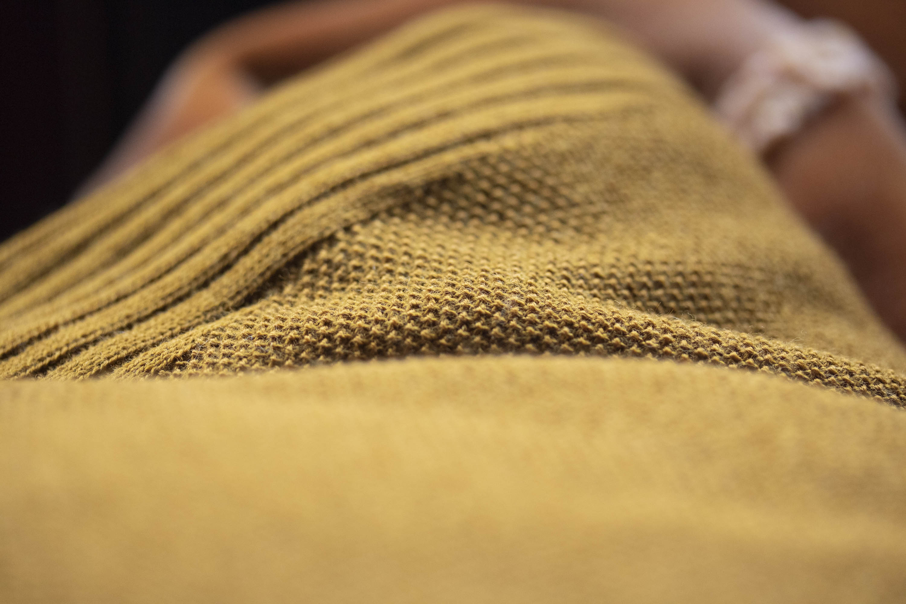 Detail of Saand holiday jumper. Fine merino yarn knitted in moss stitch for a subtle texture. Ribbed detailing. Shown in a yellow ochre