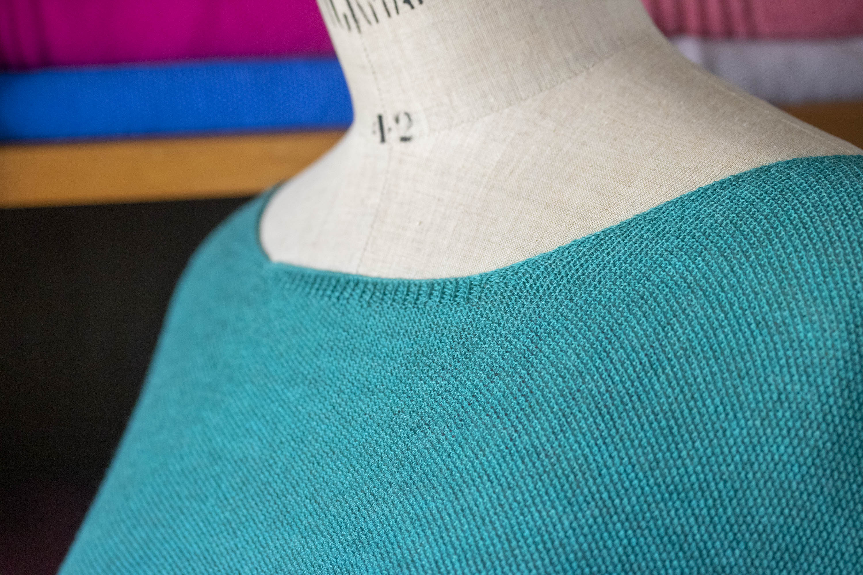 Detail of neckline on a finely knitted summer sweater with a gently scooped neck in teal yarn. Shown on a vintage mannequin.