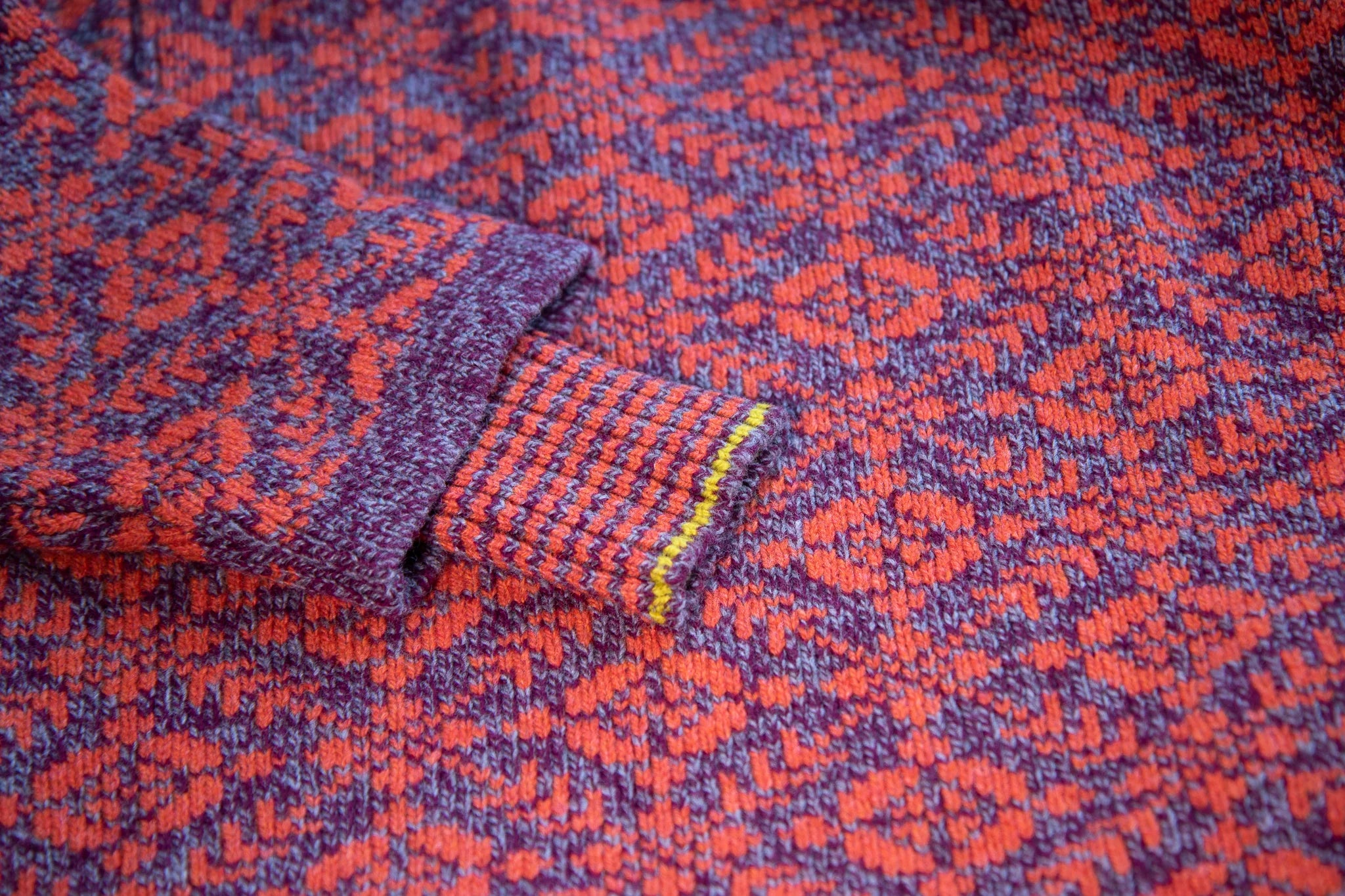 Detail of fair isle style smookie jumper with purple and pink. The cuff is inset and is striped with a yellow highlight.