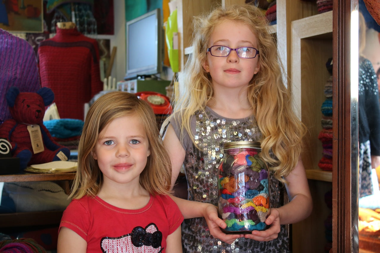 Two young girls hold a jar of cloos of yarn at the Nielanell studio, Shetland