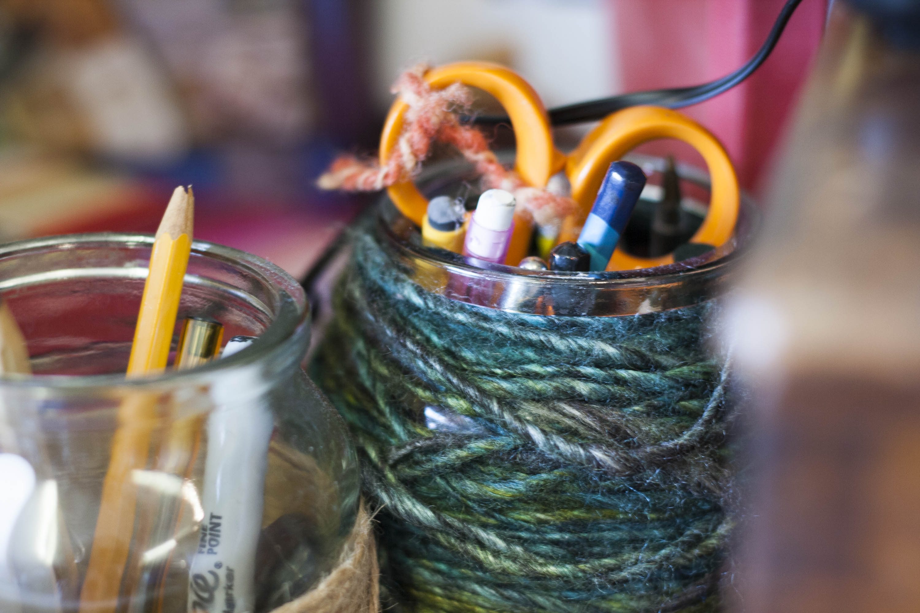 Two jam jars in the Nielanell studio, Hoswick, Shetland, with pencils, pens, scissors etc. One with teal and green handspun yarn wrapped around it
