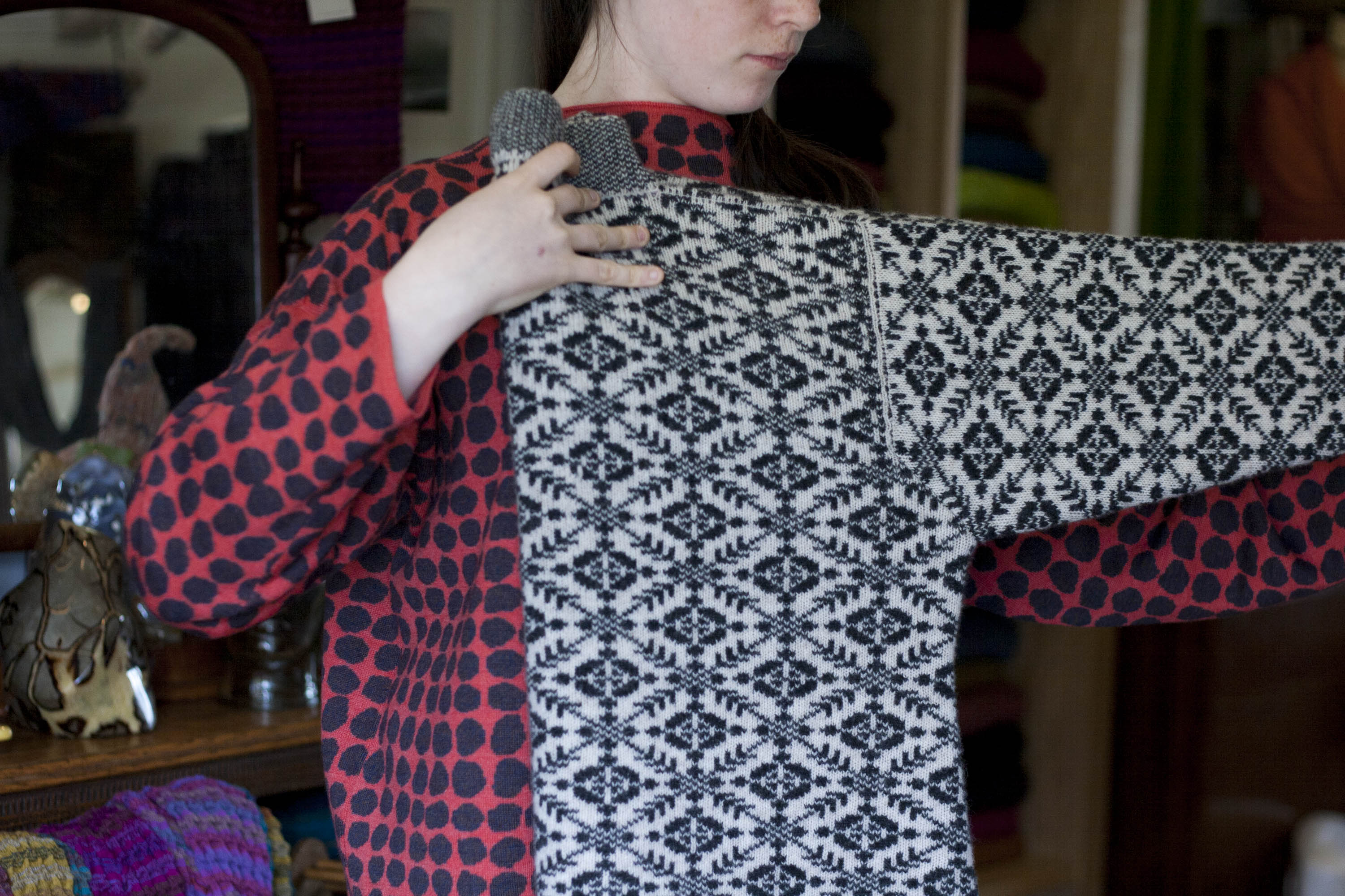 A girl holds a navy and off white patterned Fair Isle jumper by the neck and sleeve, folding it in half