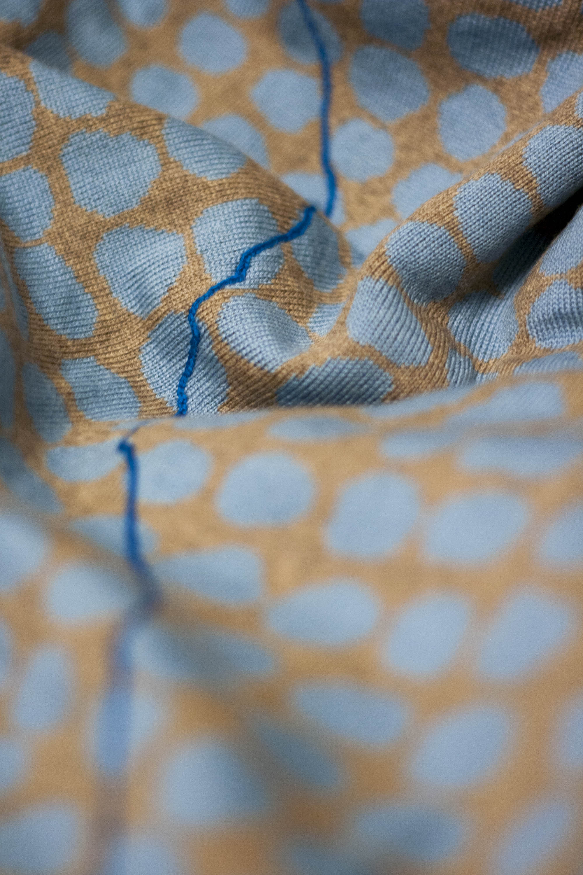 Detail of Ebb-stanes triangle jumper, knit in extra-fine merino. Shown in gold and light sky blue, with a royal blue 'drawn' line wandering over the fabric.