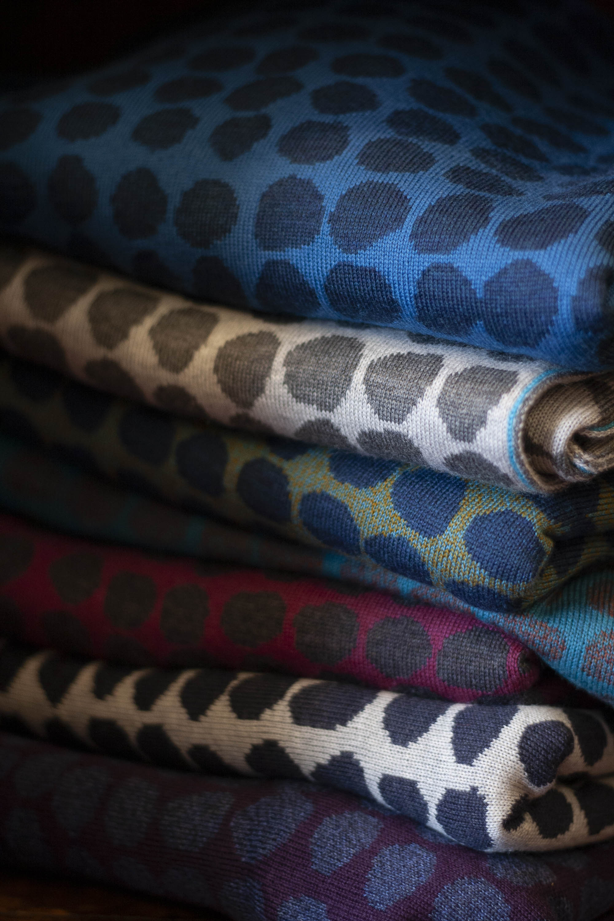A stack of contemporary Scottish knitwear in vitamin colours. Irregular dots in two colours in each pieces. Blues, greens, berry colours and neutrals