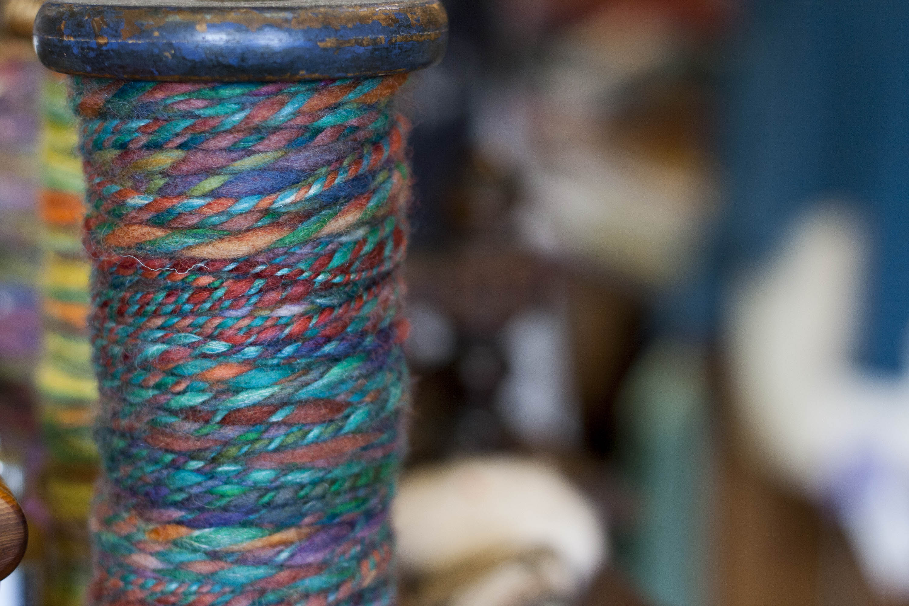 A bobbin of handspun yarn with blues, greens, oranges and reds in the two plies. Photograph taken in the Nielanell studio, Shetland