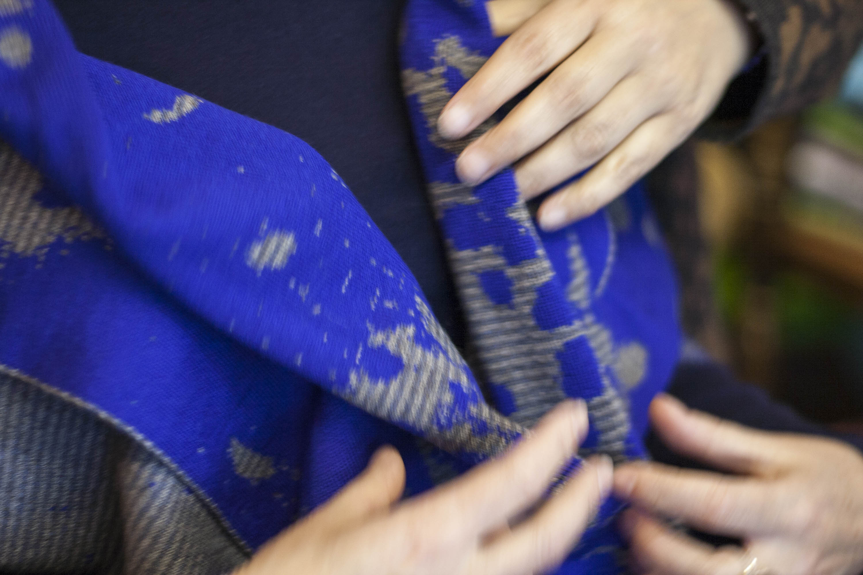 Trying on a contemporary Shetland shawl in the Nielanell studio, Hoswick, Shetland. Blue and grey abstract pattern, hands moving over