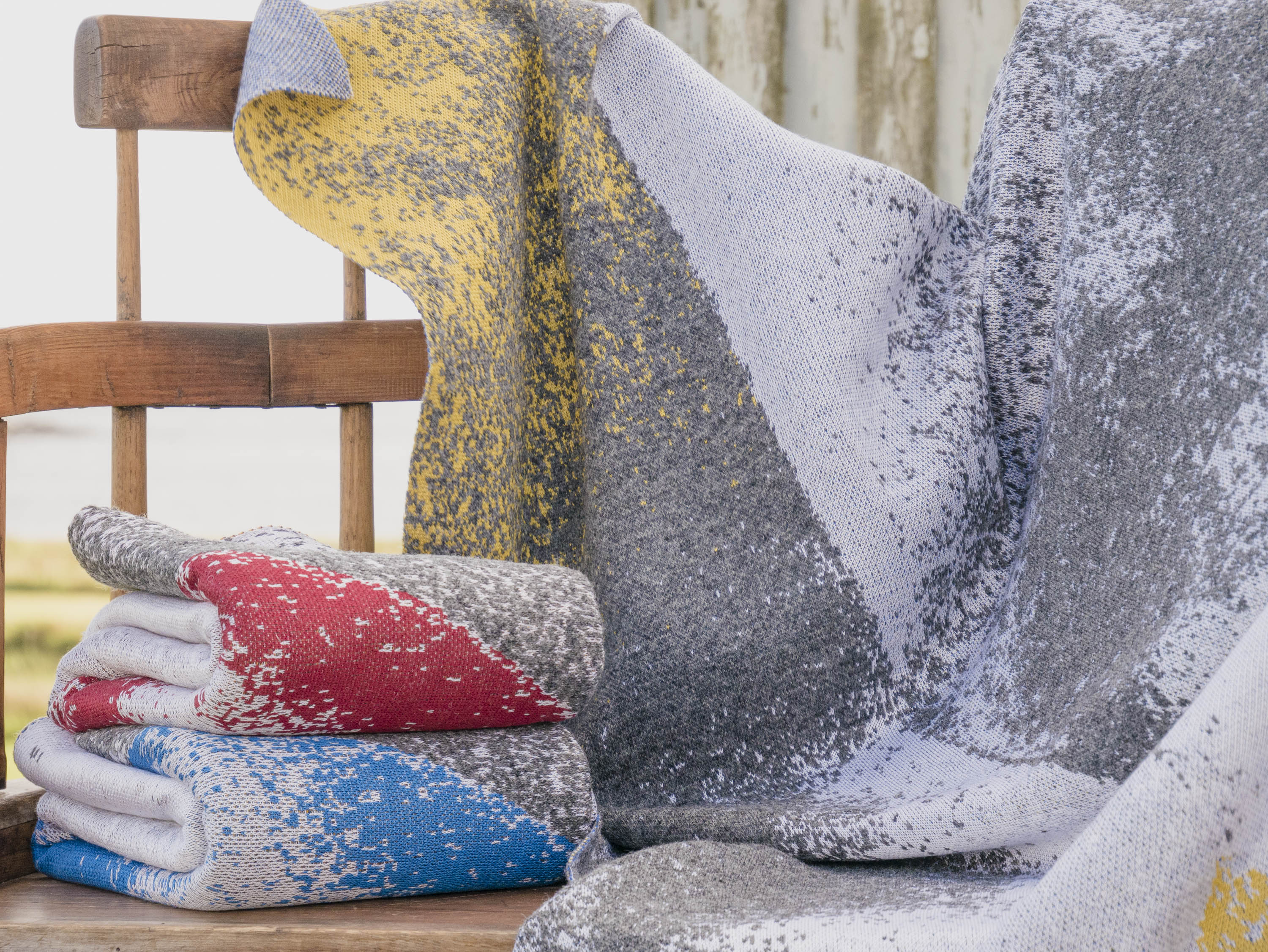 Haar Shetland blankets knitted in greys with highlight colours of blue, red or yellow. Shown draped and folded on an antique, wooden Shetland love seat.